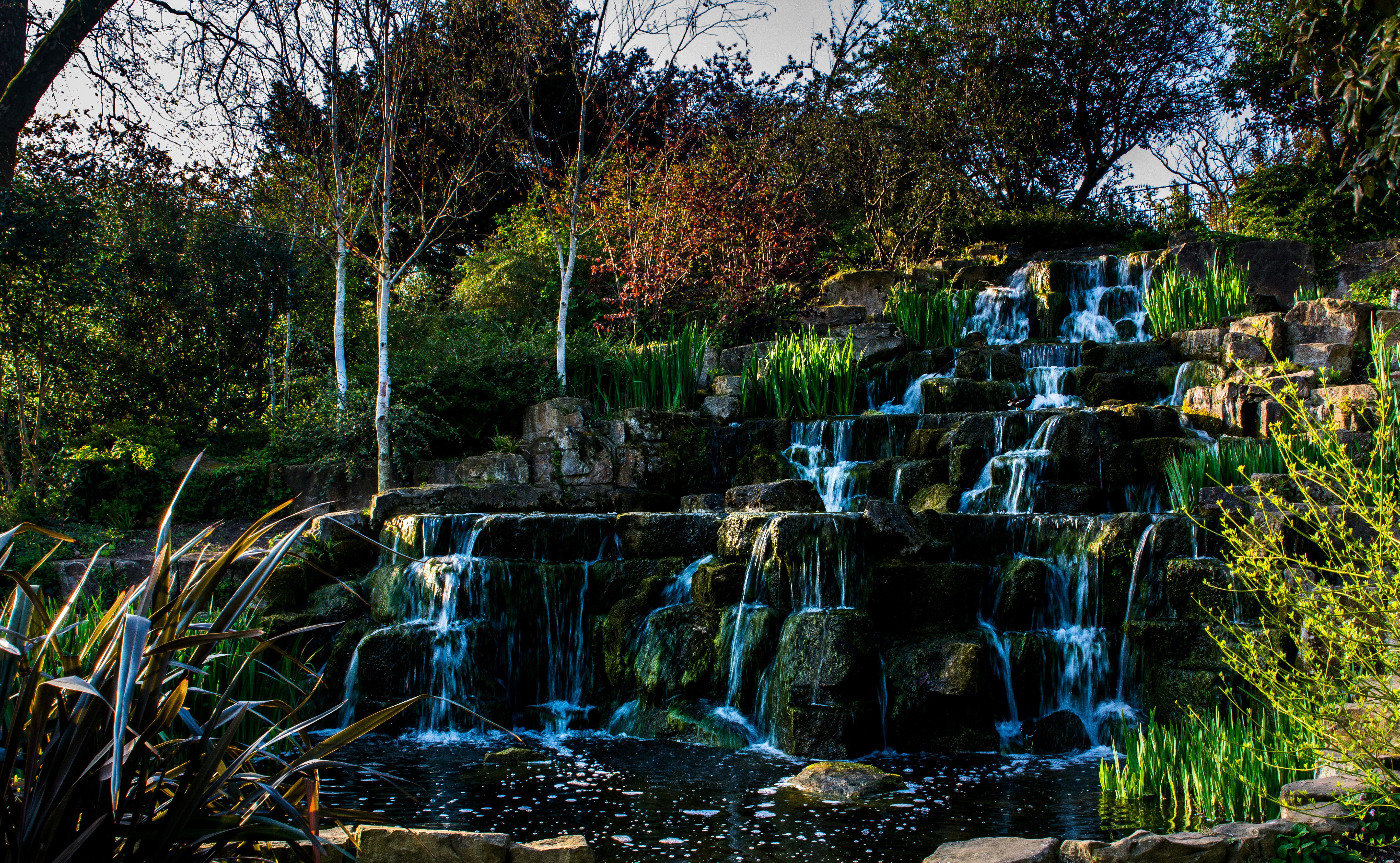 Waterfall cascading over rocks in a park HD Wallpaper
