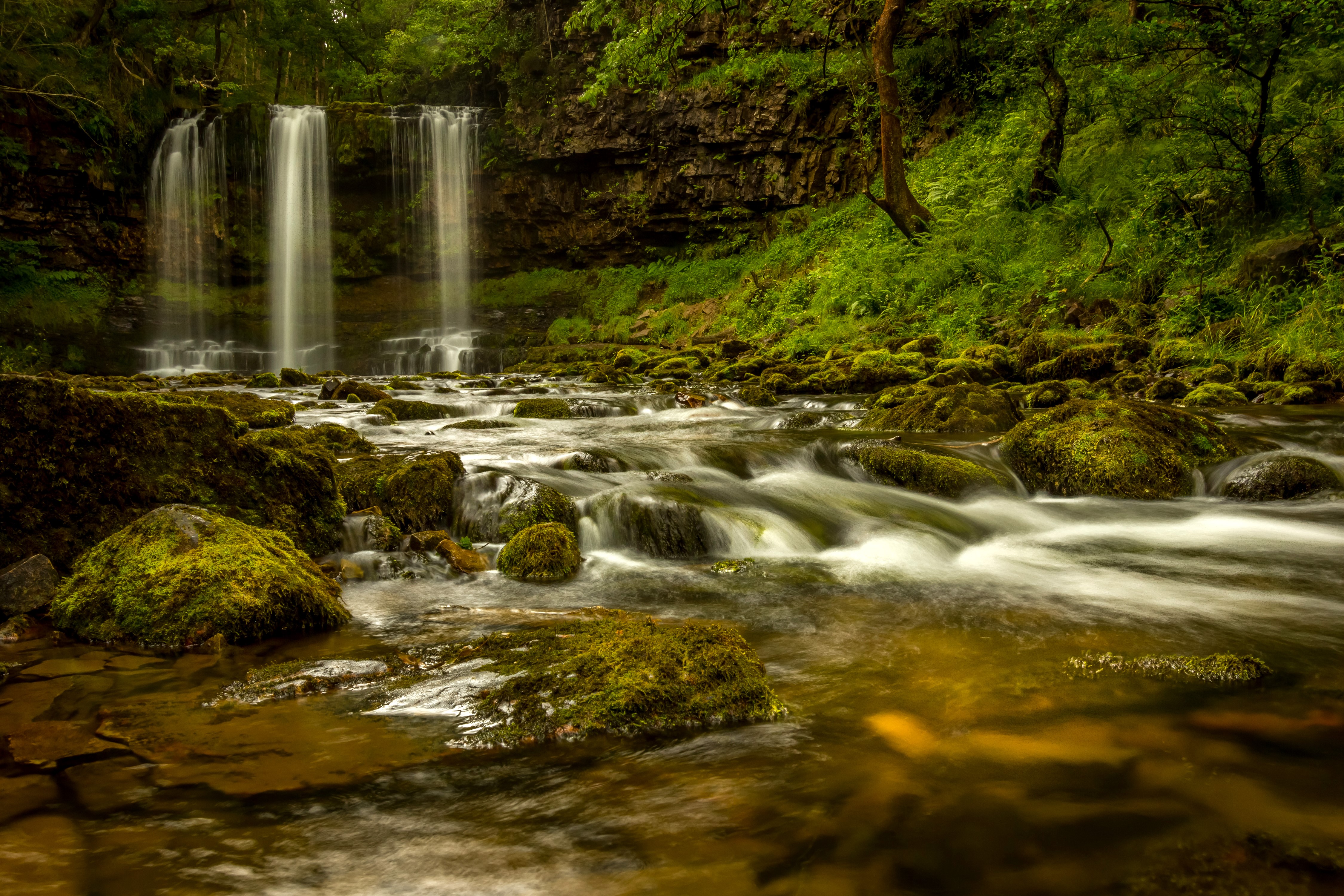 Waterfalls flowing over mossy rocks in a forest stream HD Wallpaper