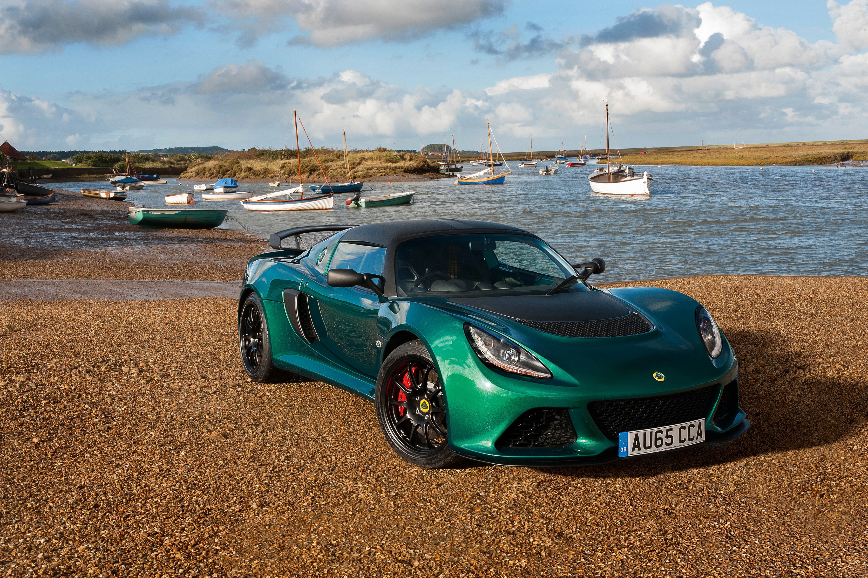 Green Lotus Exige Sport 350 parked by a coast with boats HD Wallpaper