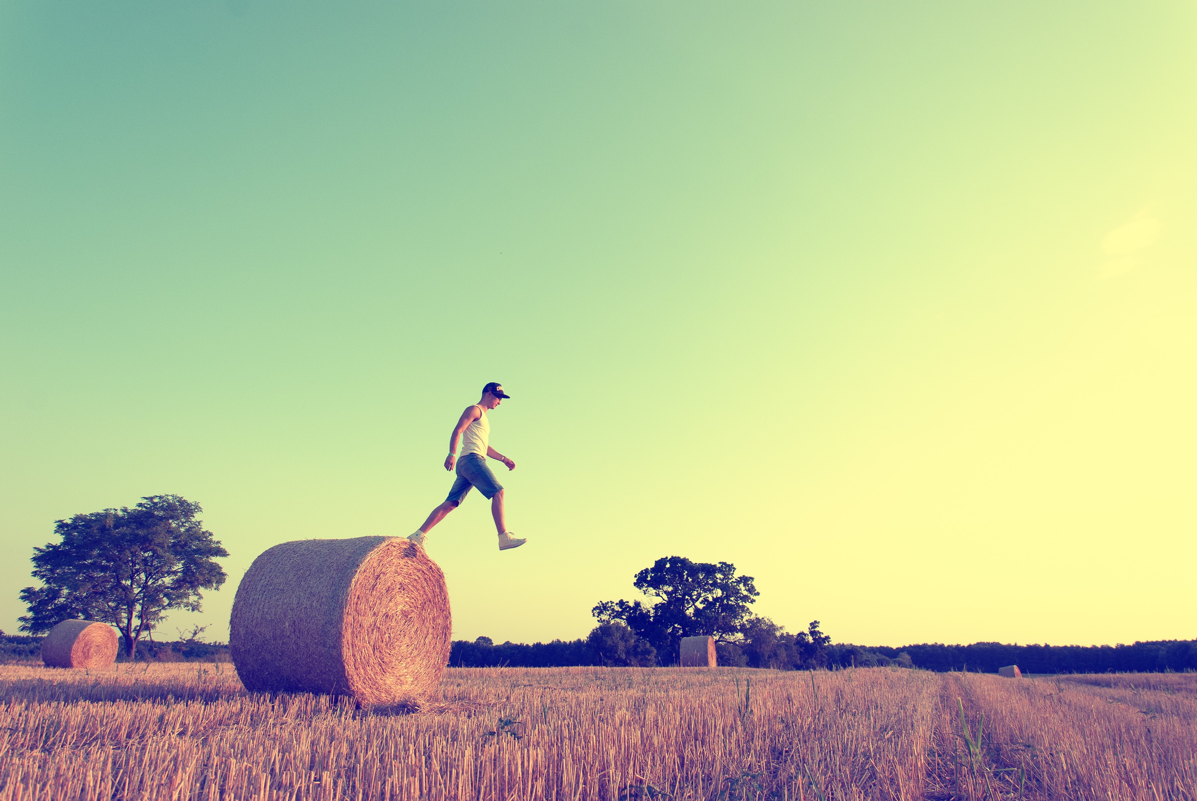 Man jumping over hay bale in field HD Wallpaper