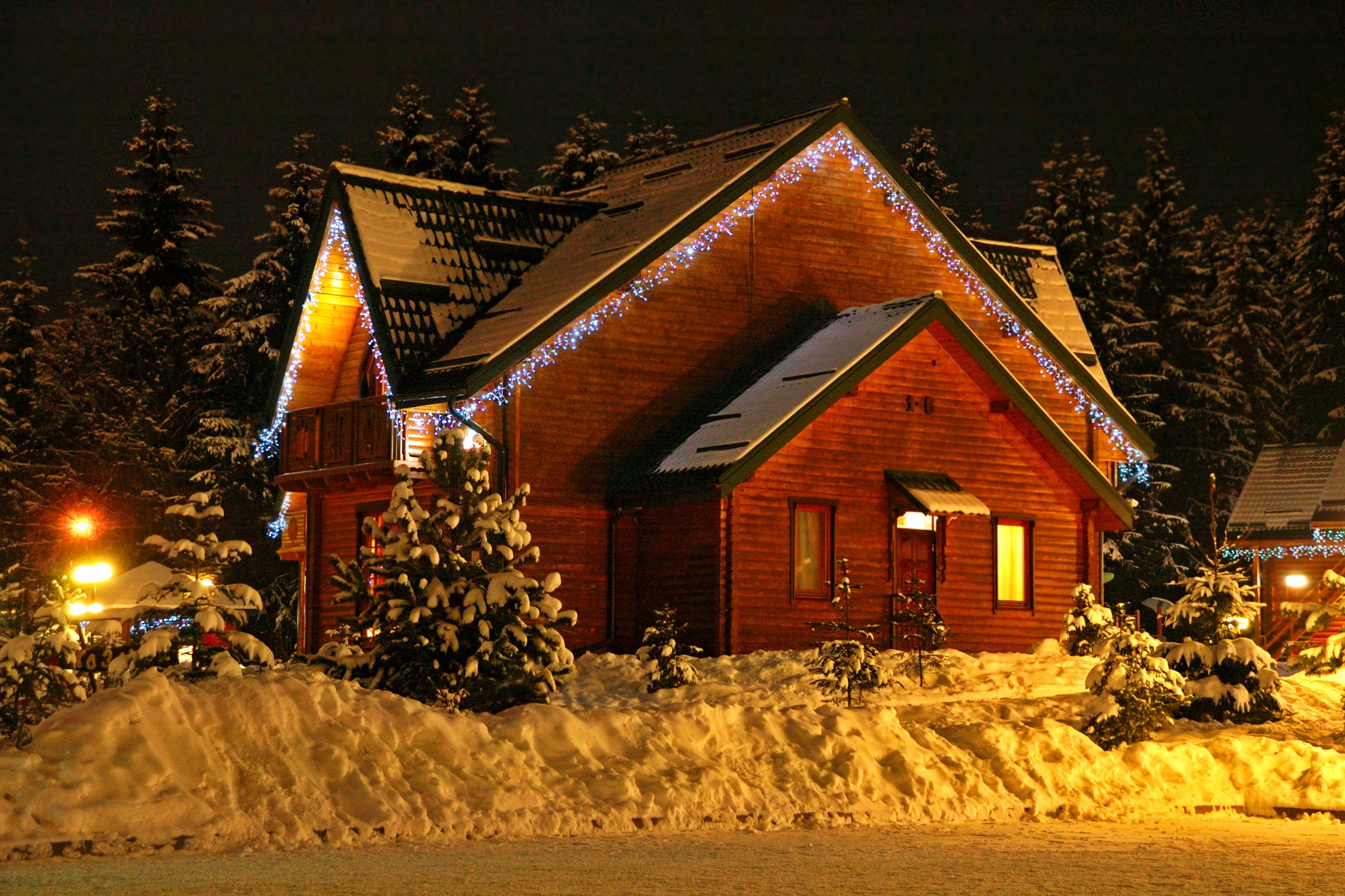 Wooden houses decorated with fairy lights in the snow at night HD Wallpaper