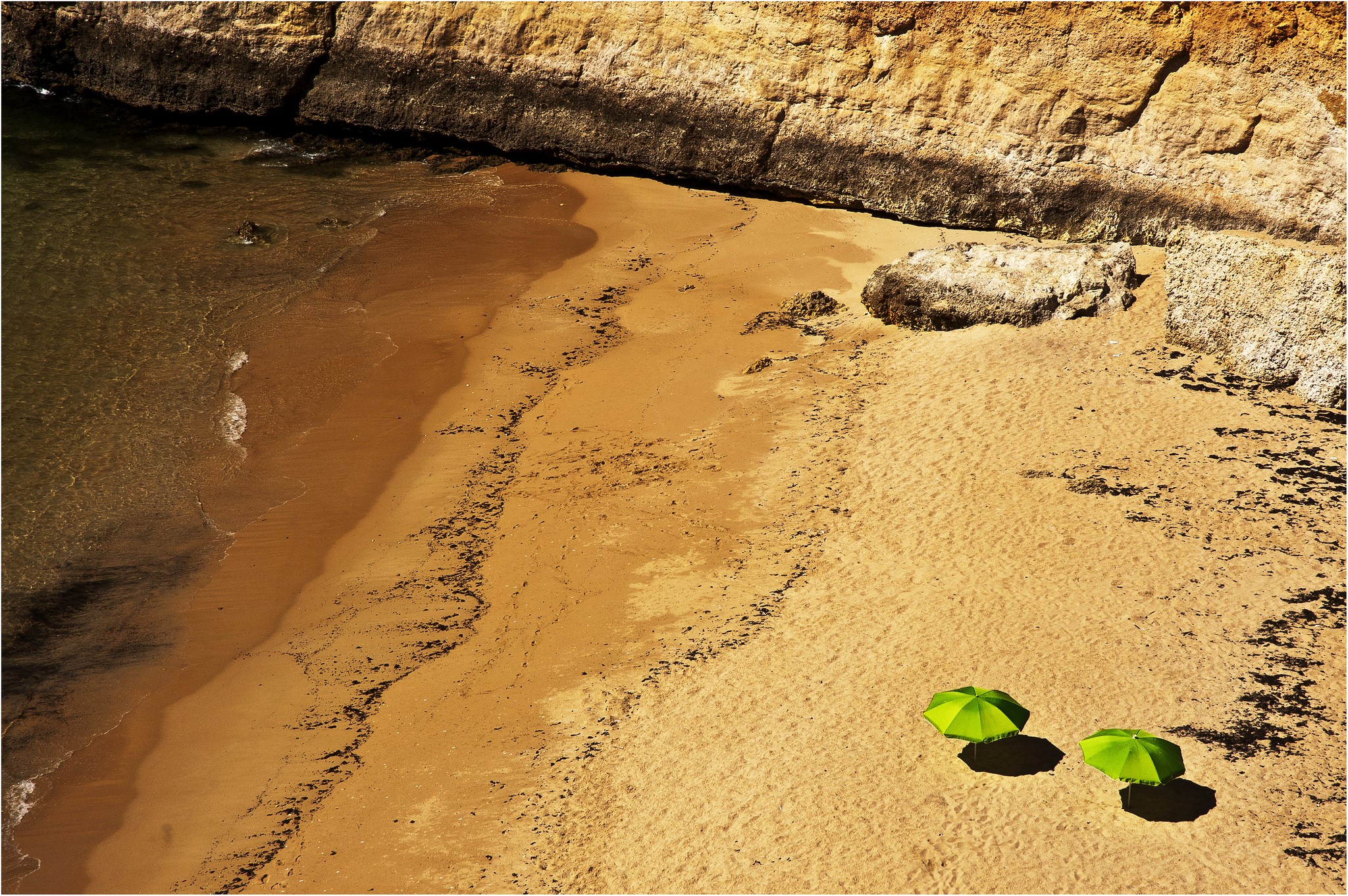 Two green umbrellas on a sandy beach next to a rocky cliff HD Wallpaper