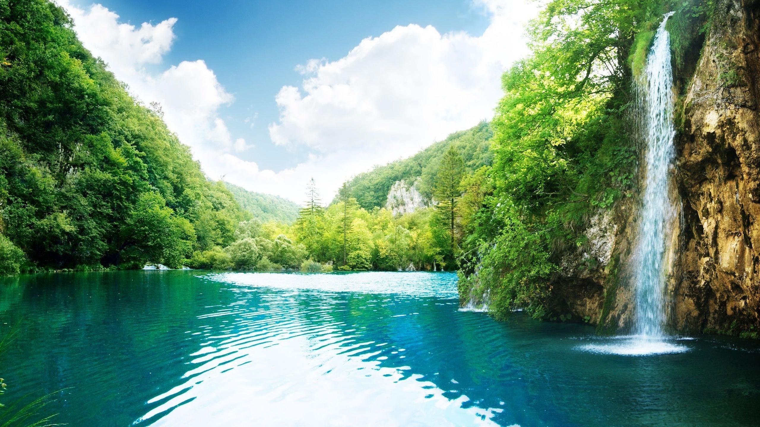 Waterfall cascading into a turquoise lake surrounded by green trees HD Wallpaper