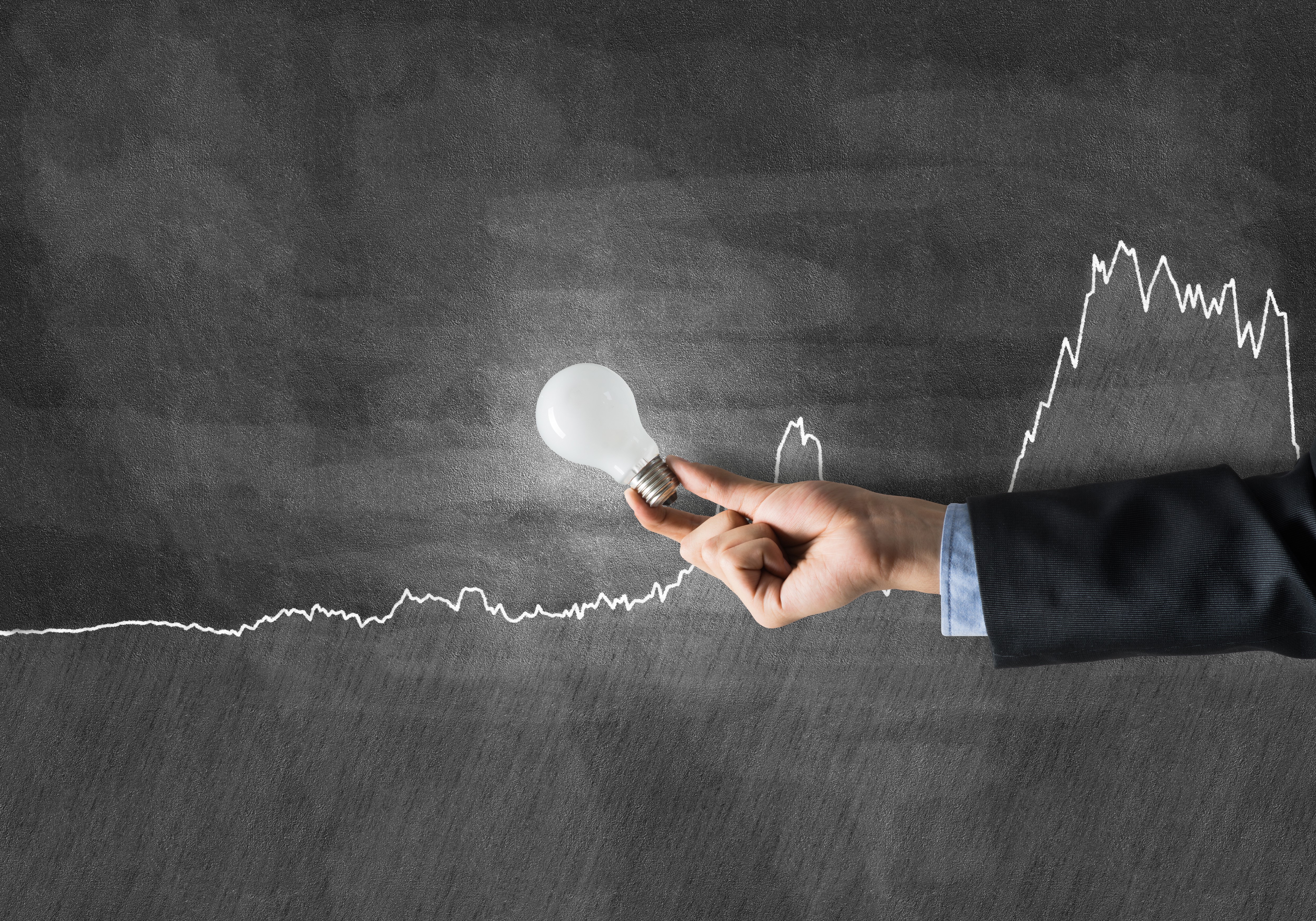 Hand holding light bulb over graph on chalkboard HD Wallpaper
