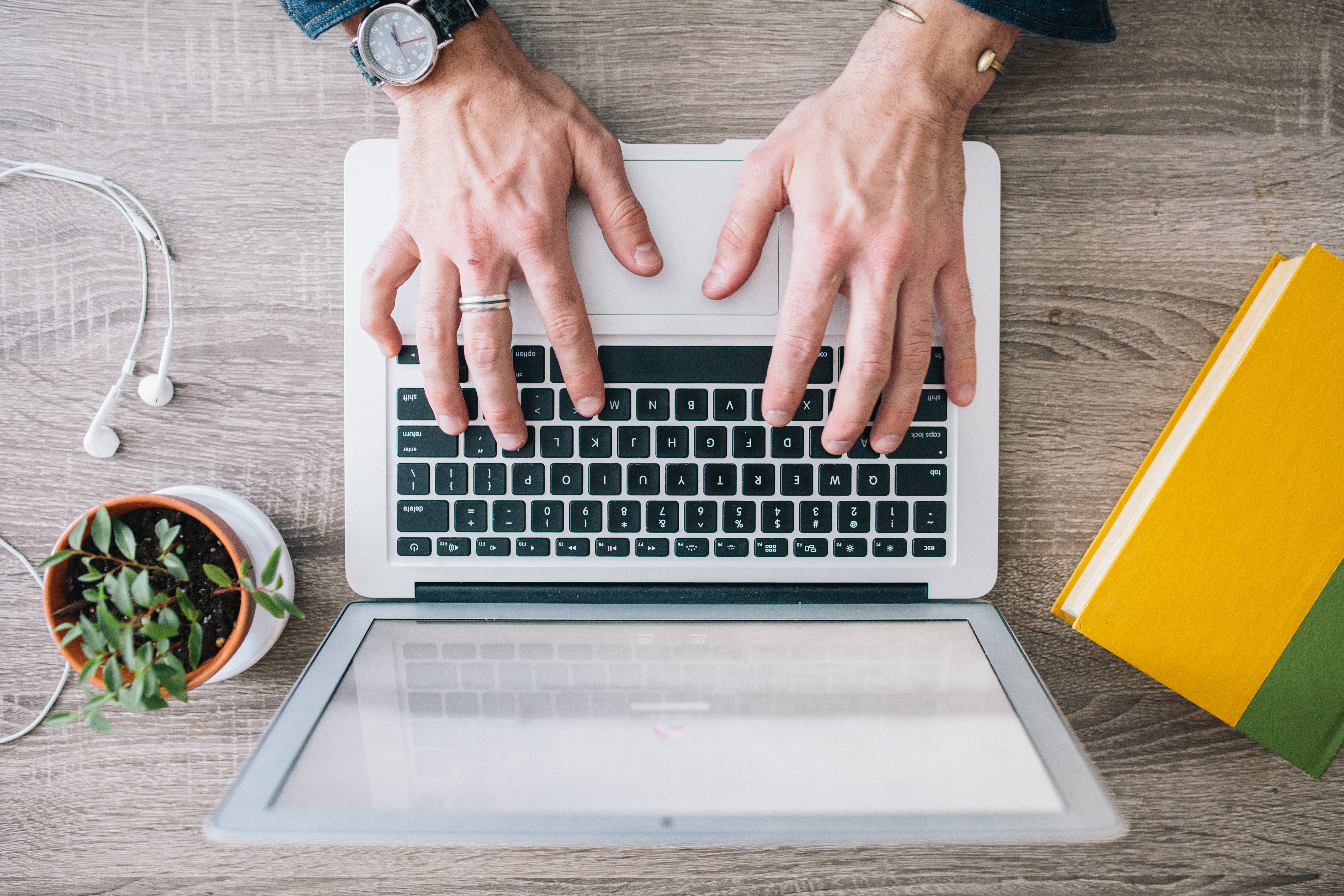 Hands typing on a laptop with a book and plant HD Wallpaper