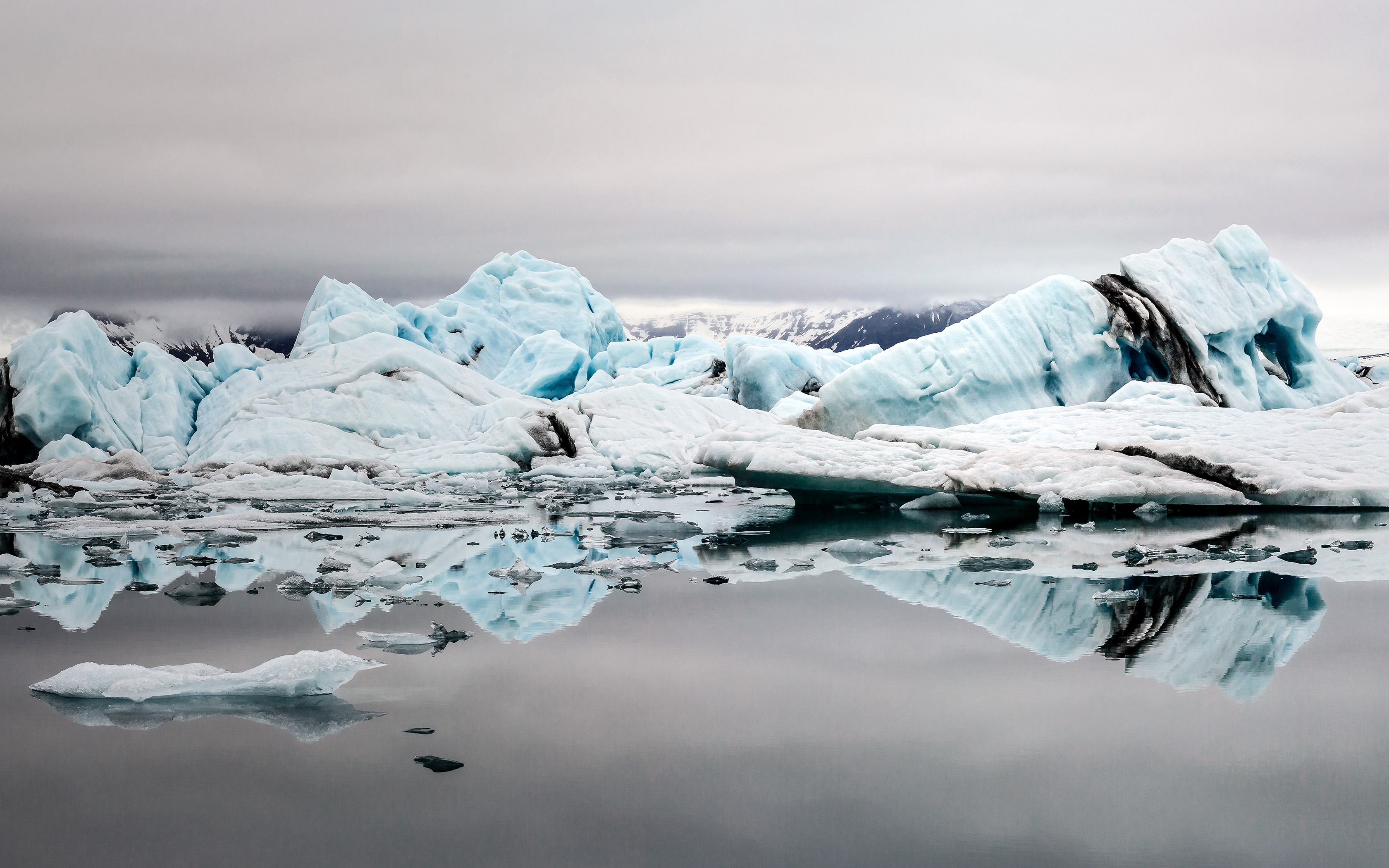Icebergs floating in glacial lagoon with mountains HD Wallpaper