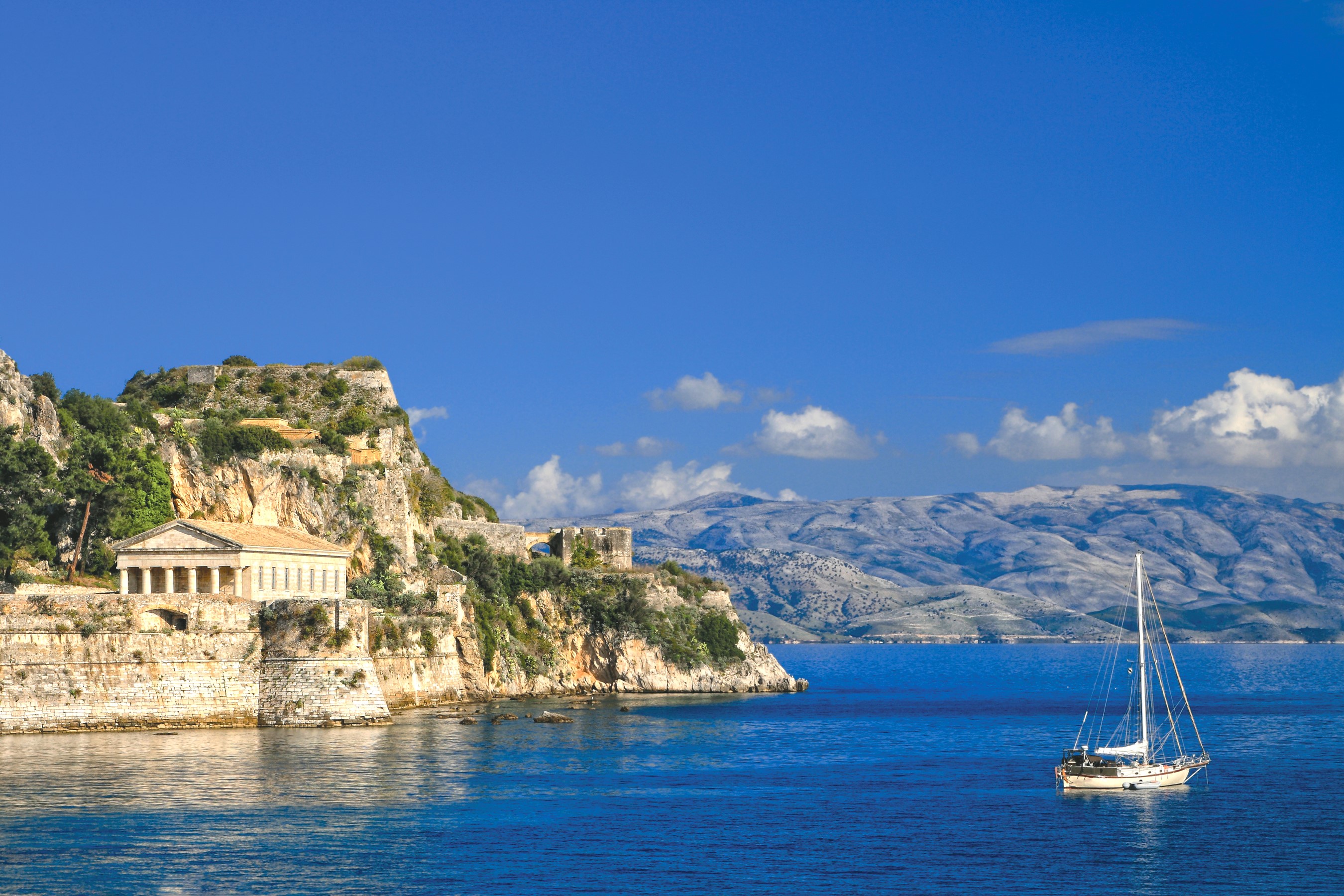 Ancient ruins on a cliff overlooking the sea with a sailboat HD Wallpaper