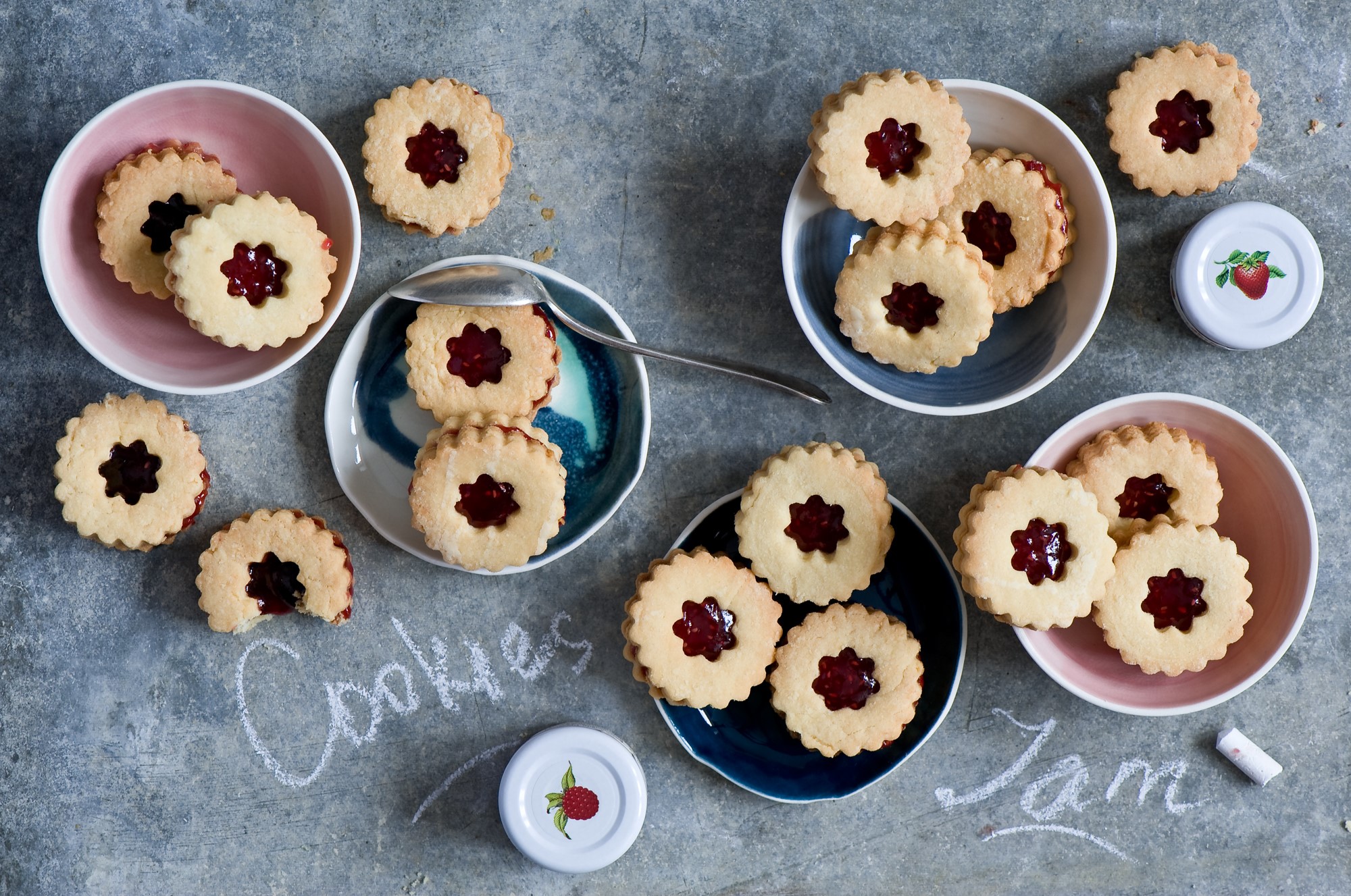 Jam-filled cookies arranged in bowls and on a surface HD Wallpaper