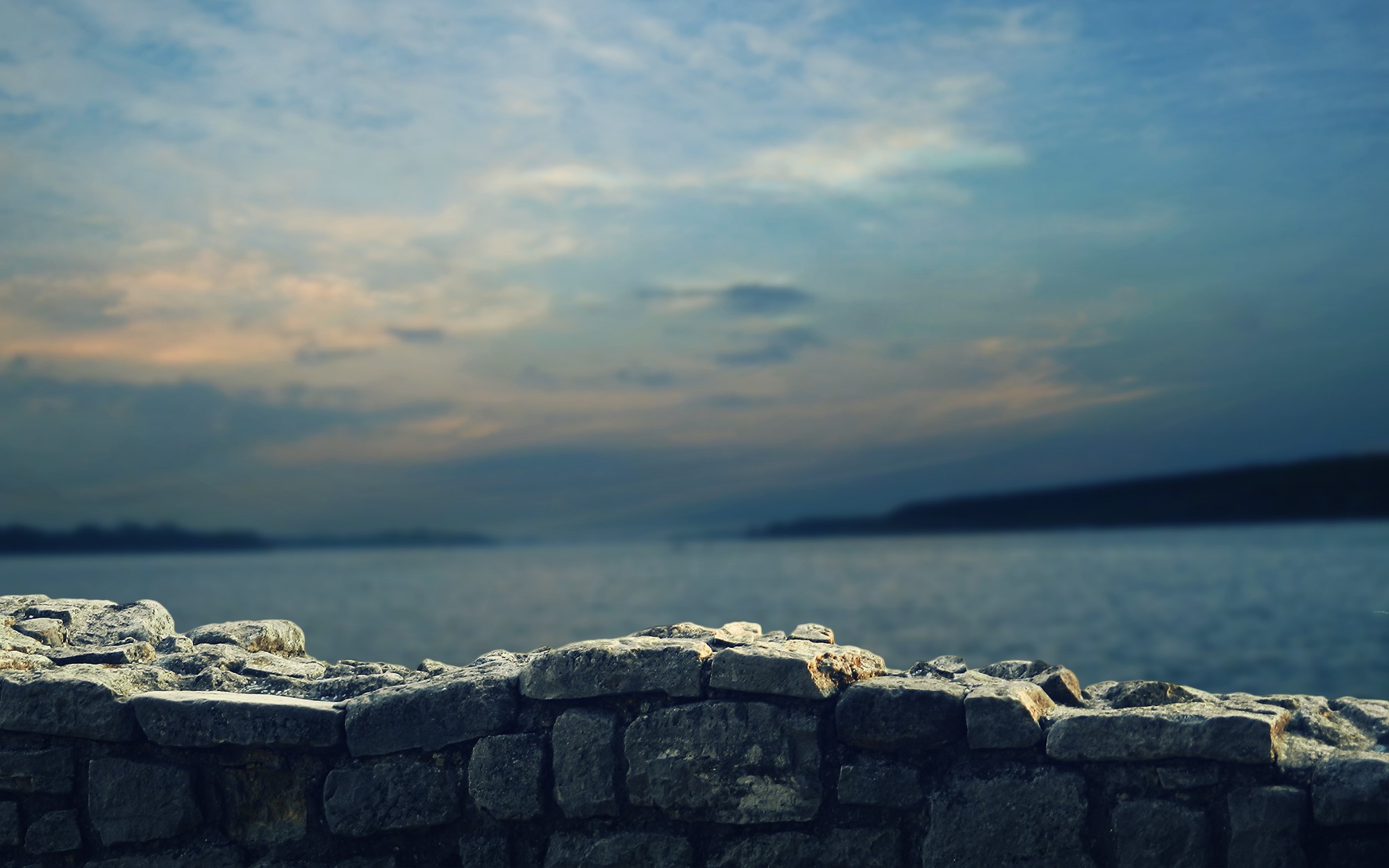 Stone wall overlooking a body of water at dusk HD Wallpaper