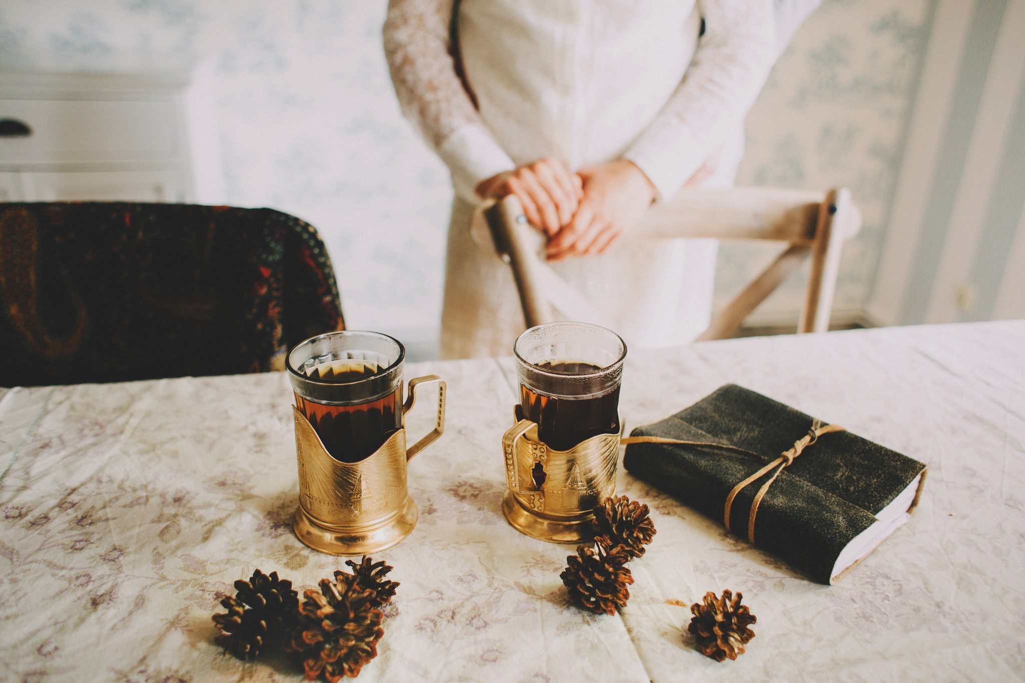 Two glasses of tea, pine cones, and a book on a table HD Wallpaper