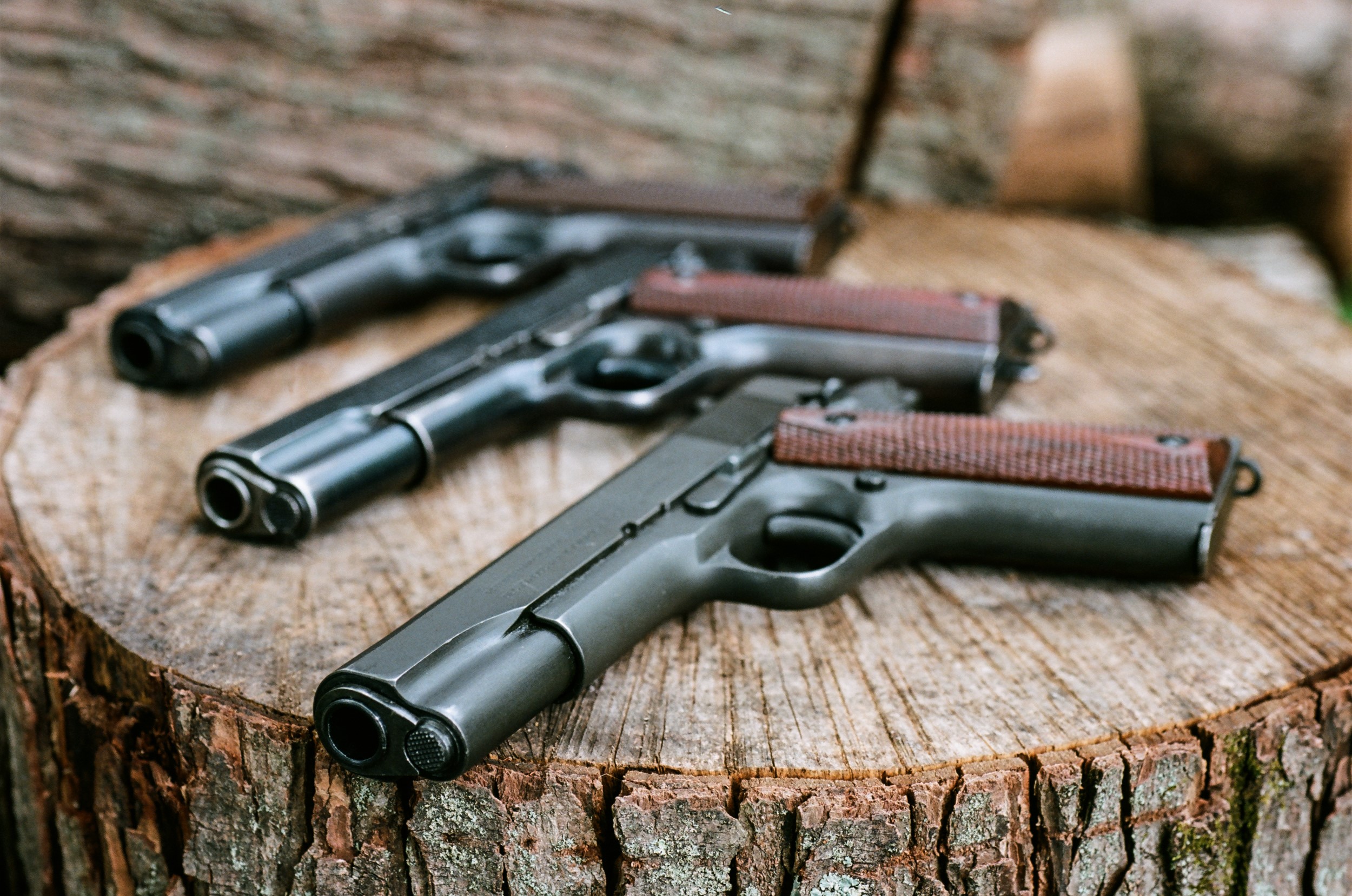 Three Colt 1911 pistols on a tree stump HD Wallpaper