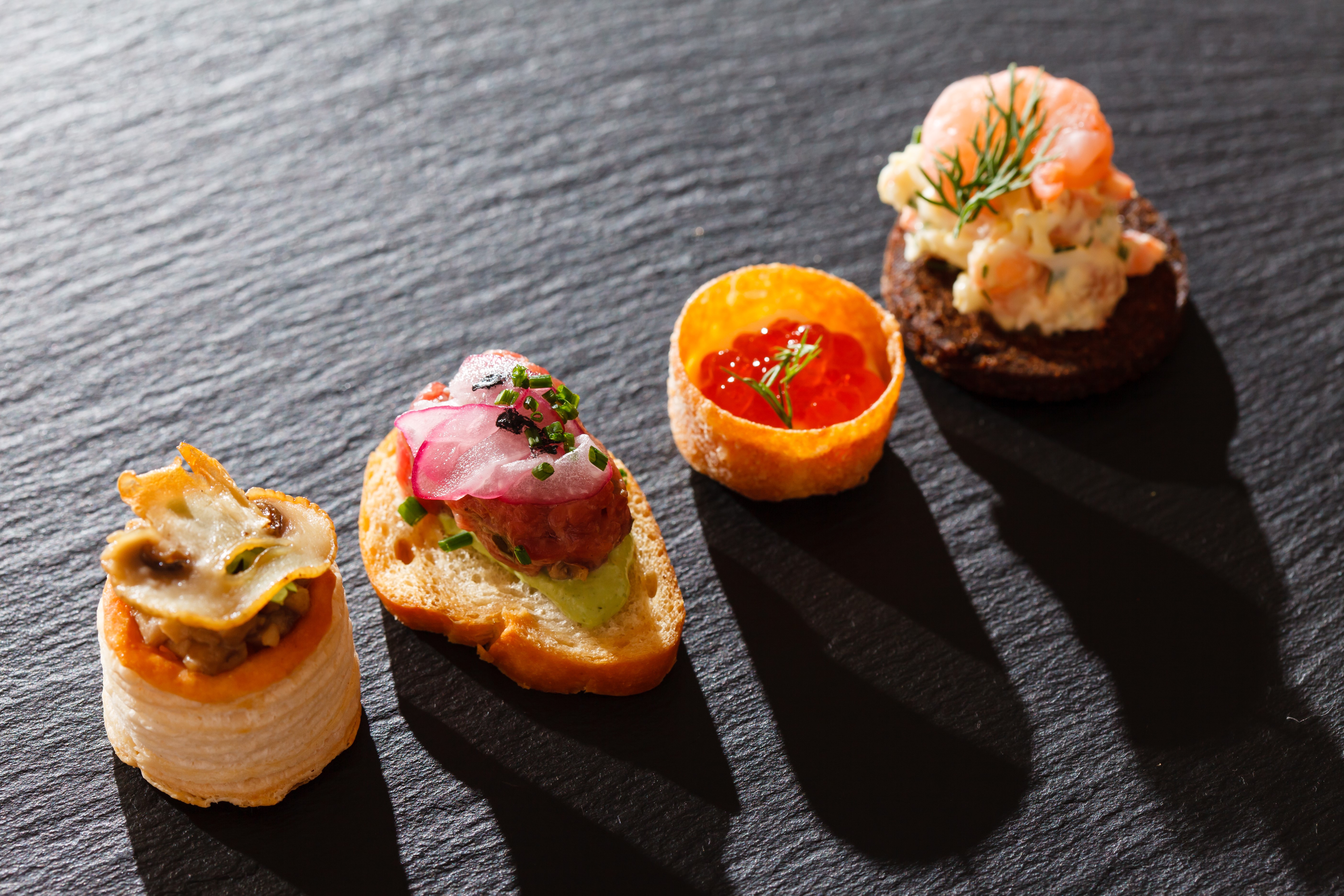 Assortment of gourmet appetizers on a dark slate surface HD Wallpaper