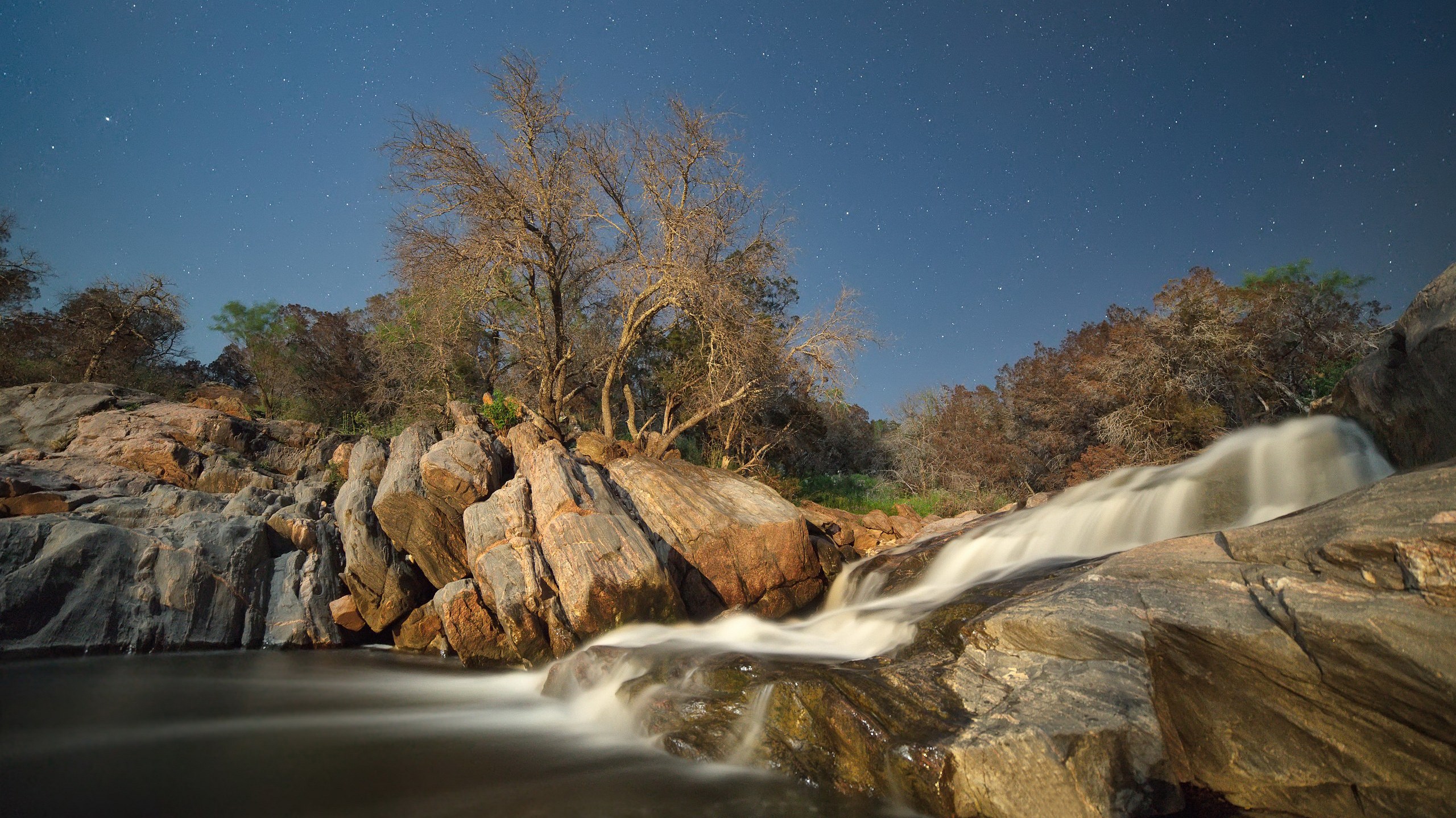Waterfall flowing over rocks under a starry night sky HD Wallpaper
