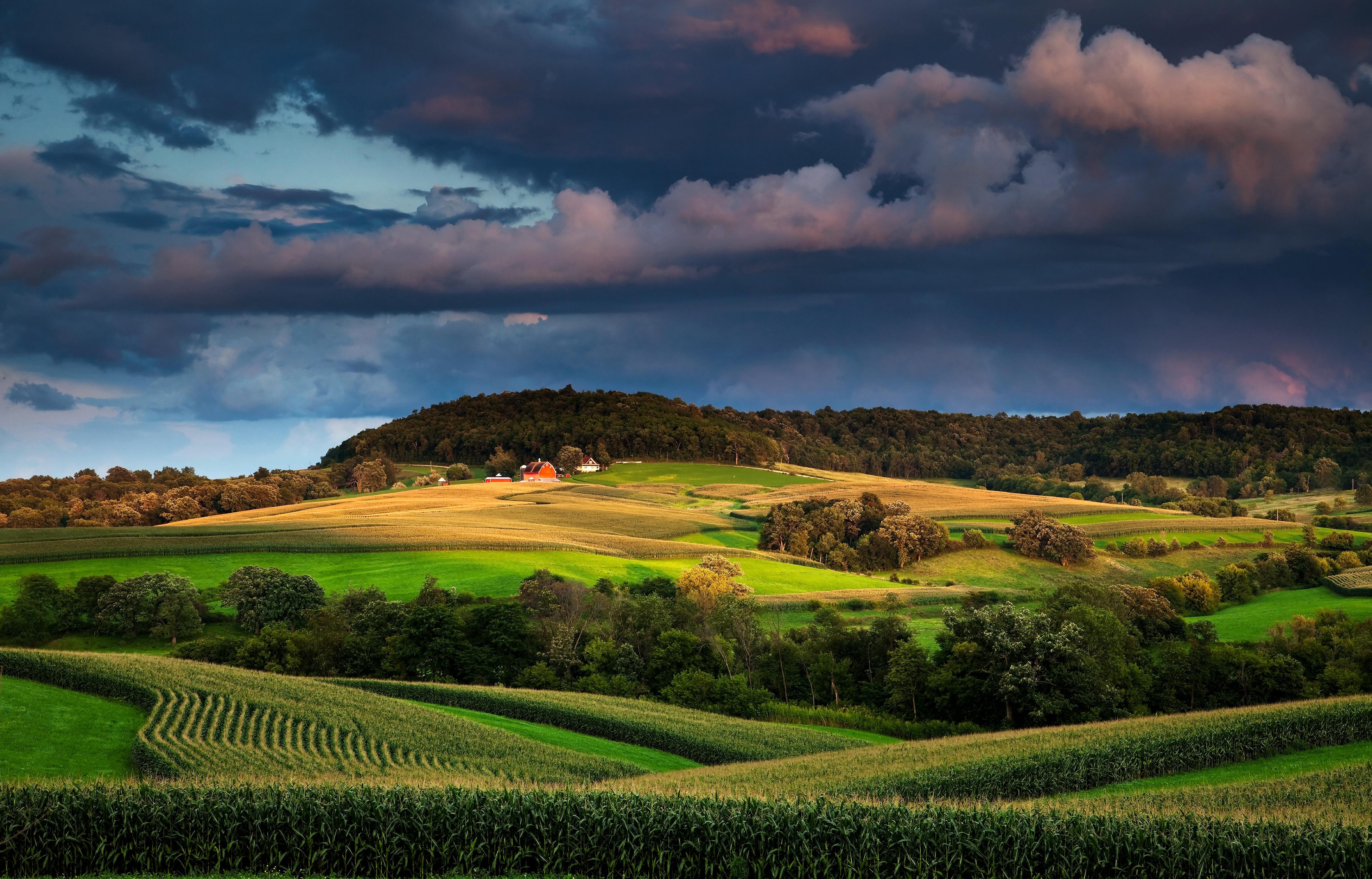 Farm fields and rolling hills under stormy sky HD Wallpaper
