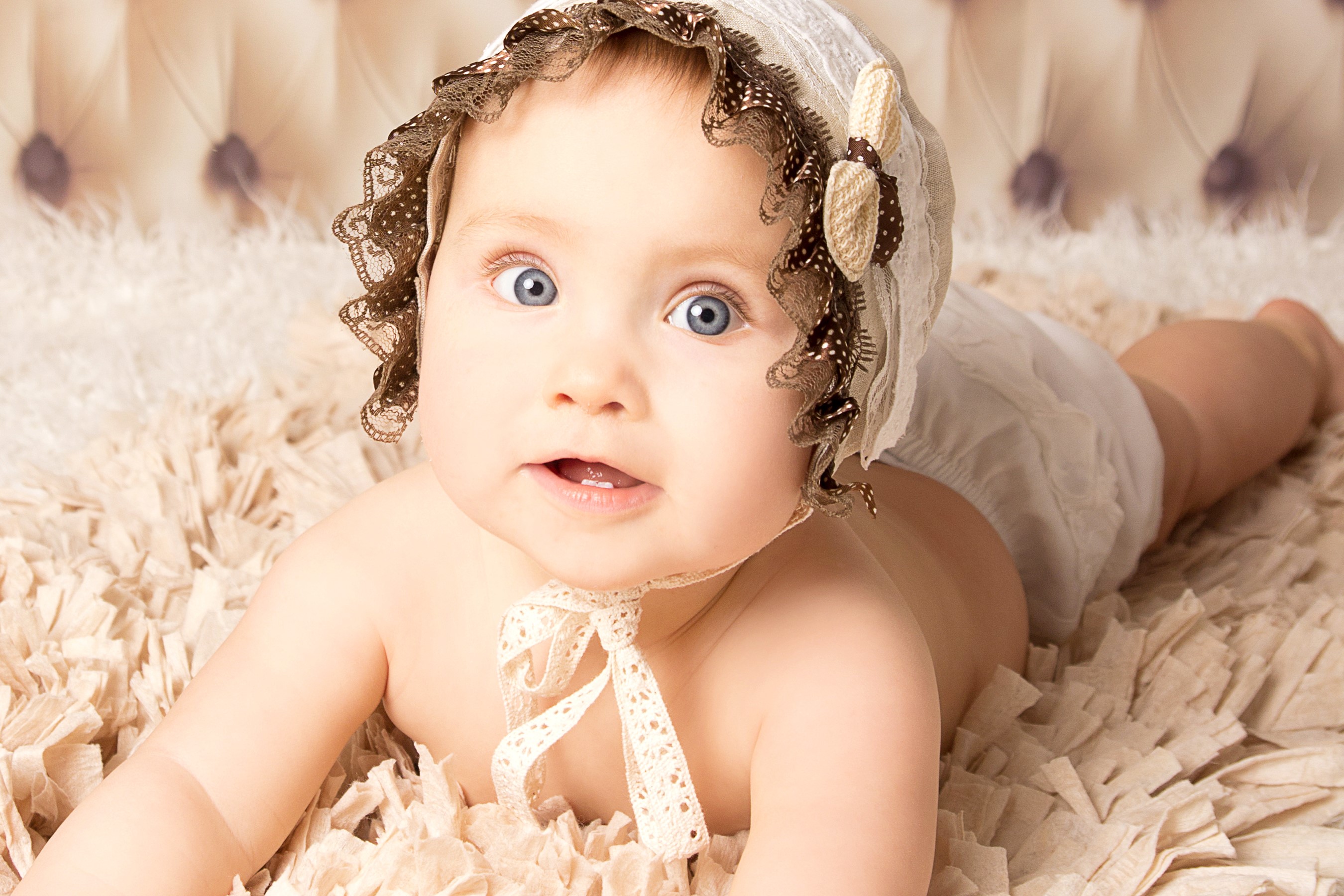 Baby wearing a bonnet lying on a fluffy rug HD Wallpaper