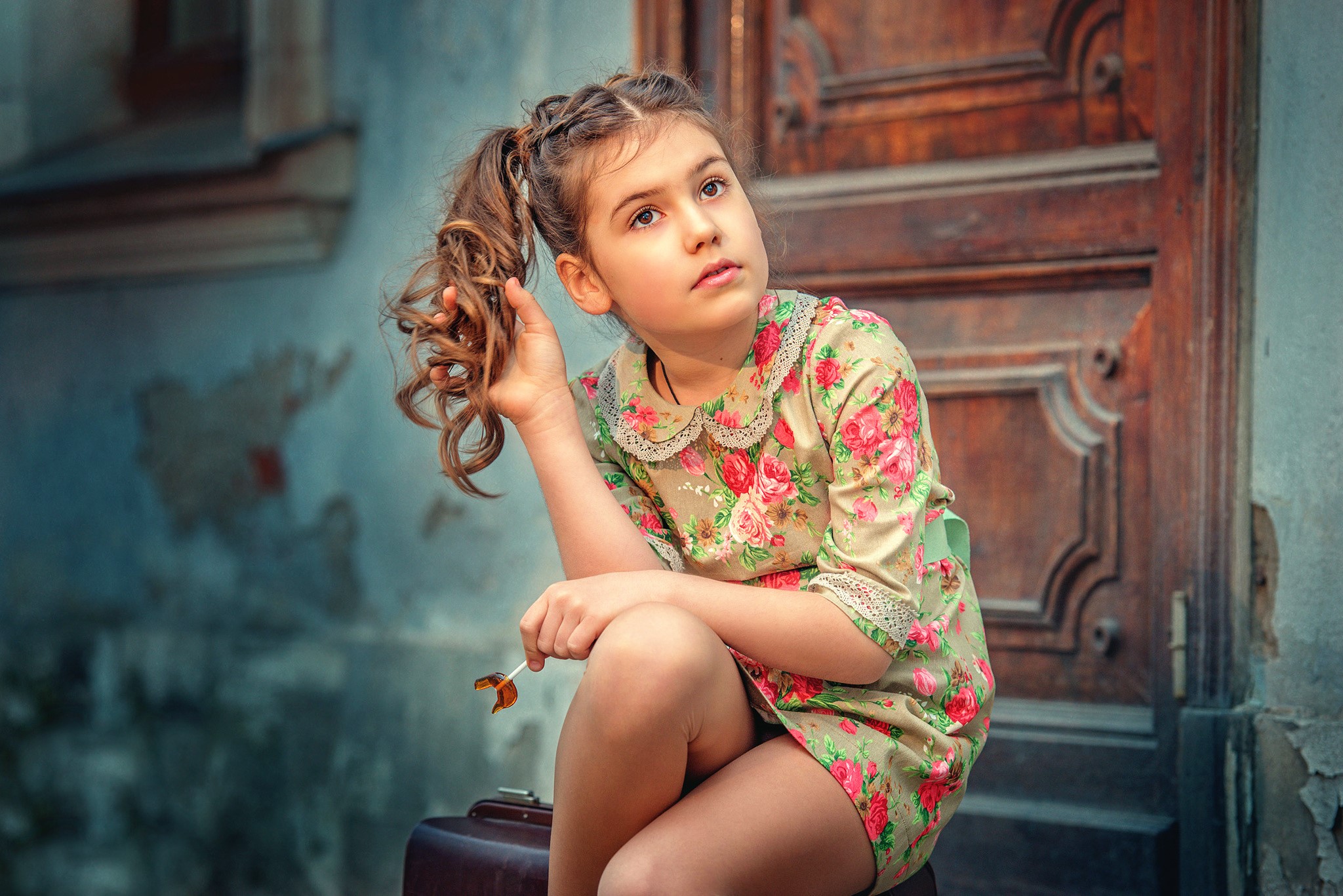 Young girl with a lollipop sitting on a suitcase HD Wallpaper