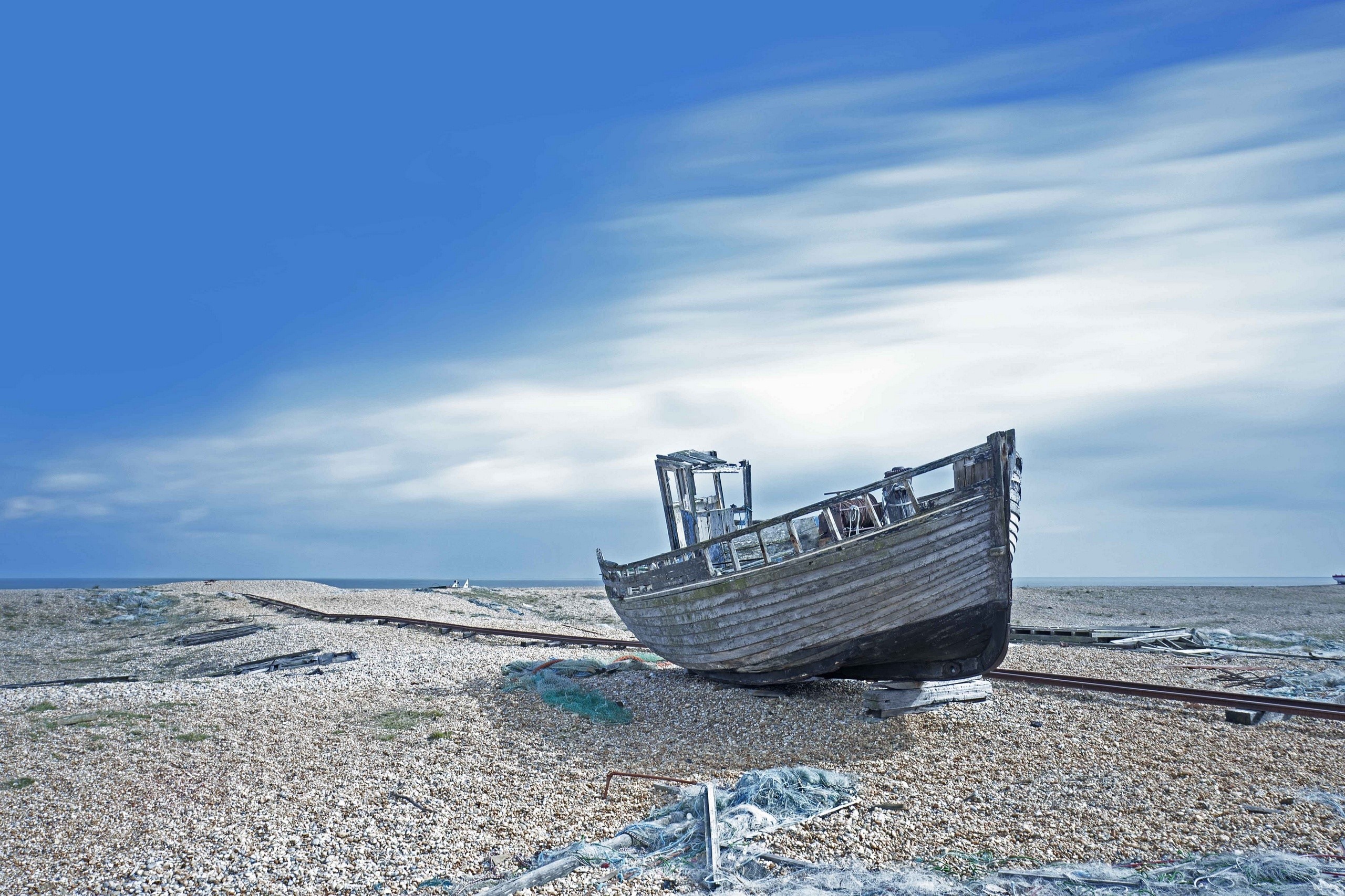 Abandoned boat on a pebble beach under a blue sky HD Wallpaper