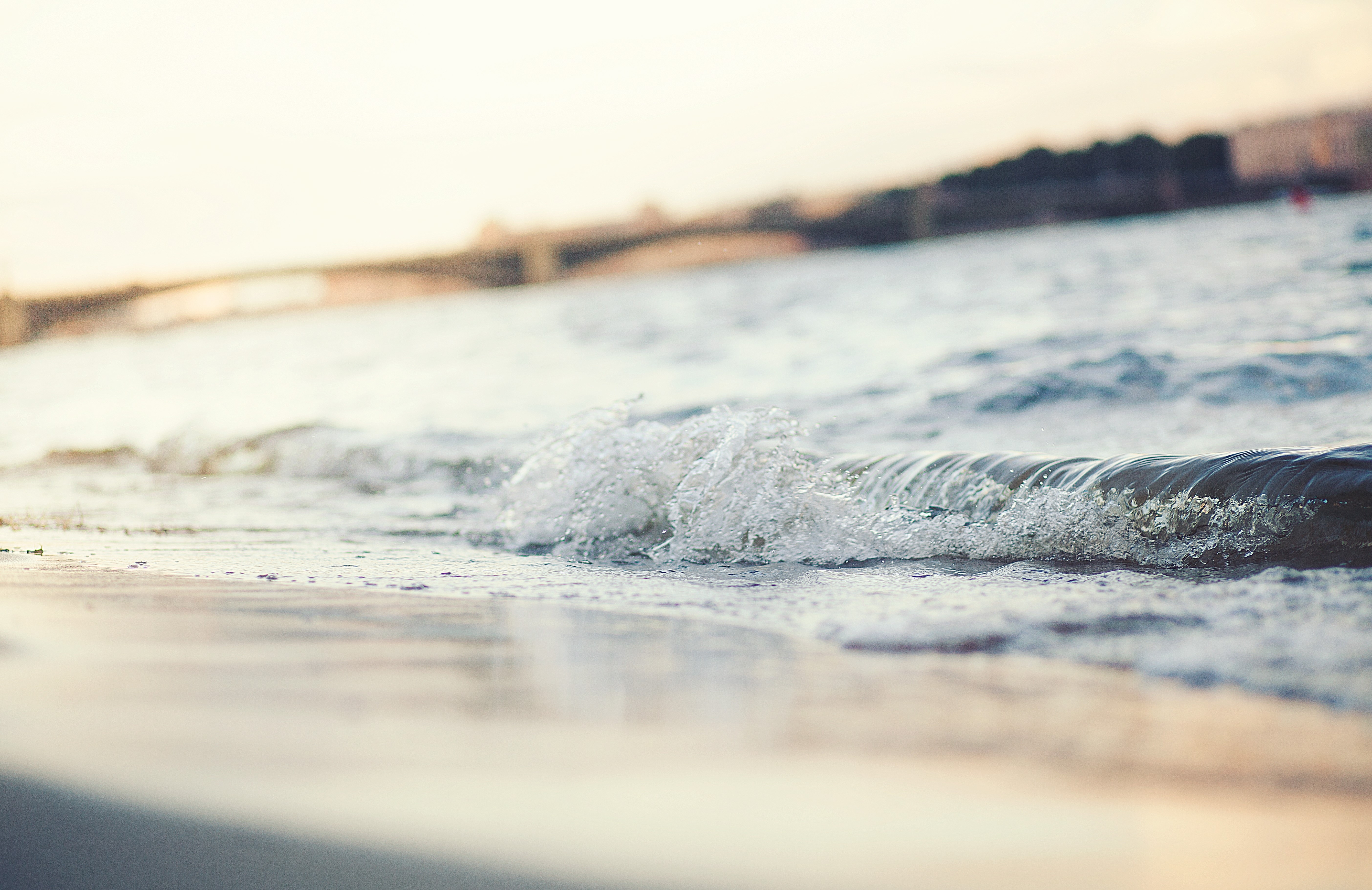 Waves crashing on a sandy shore with a bridge in the background HD Wallpaper