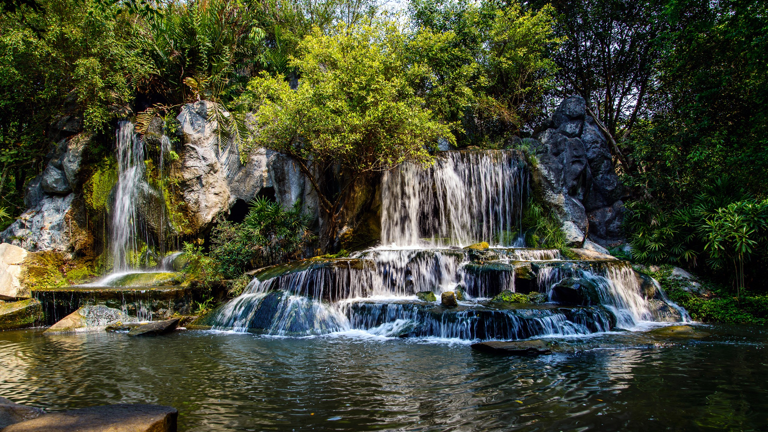 Multi-tiered waterfall cascading over rocks into a pool HD Wallpaper