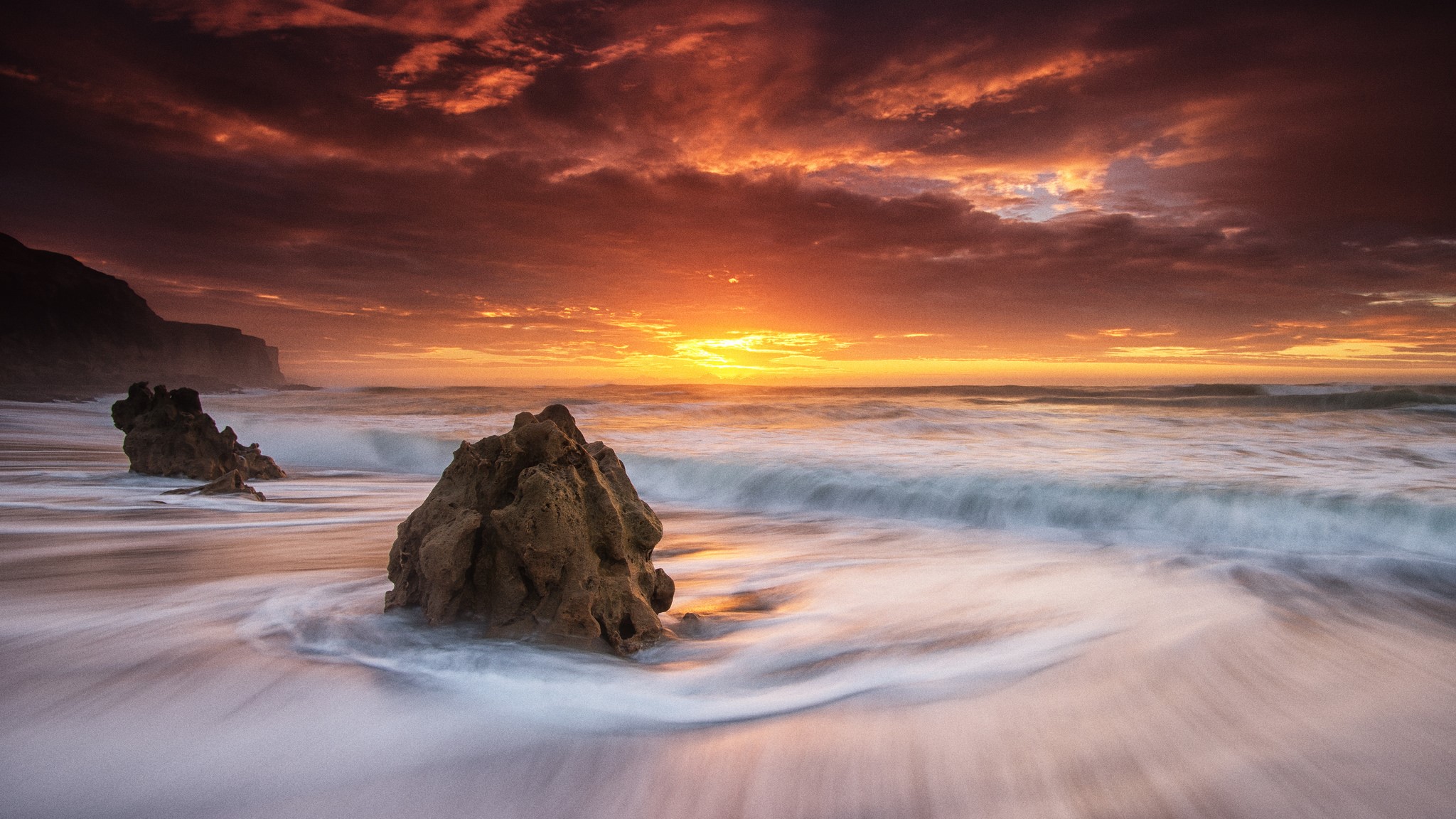 Sunset over the ocean with rocks on the shore HD Wallpaper