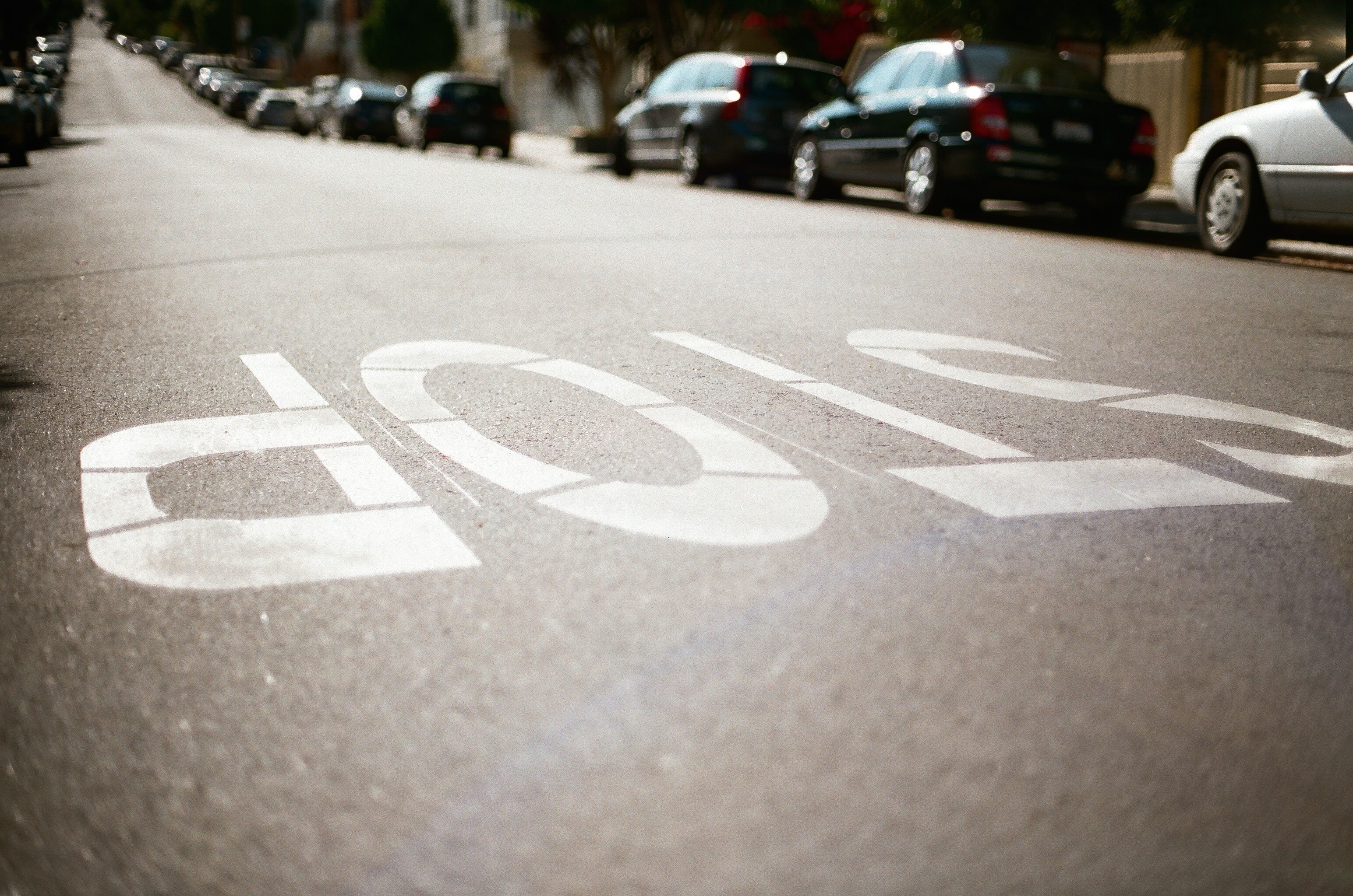 Stop sign painted on asphalt road with cars parked HD Wallpaper