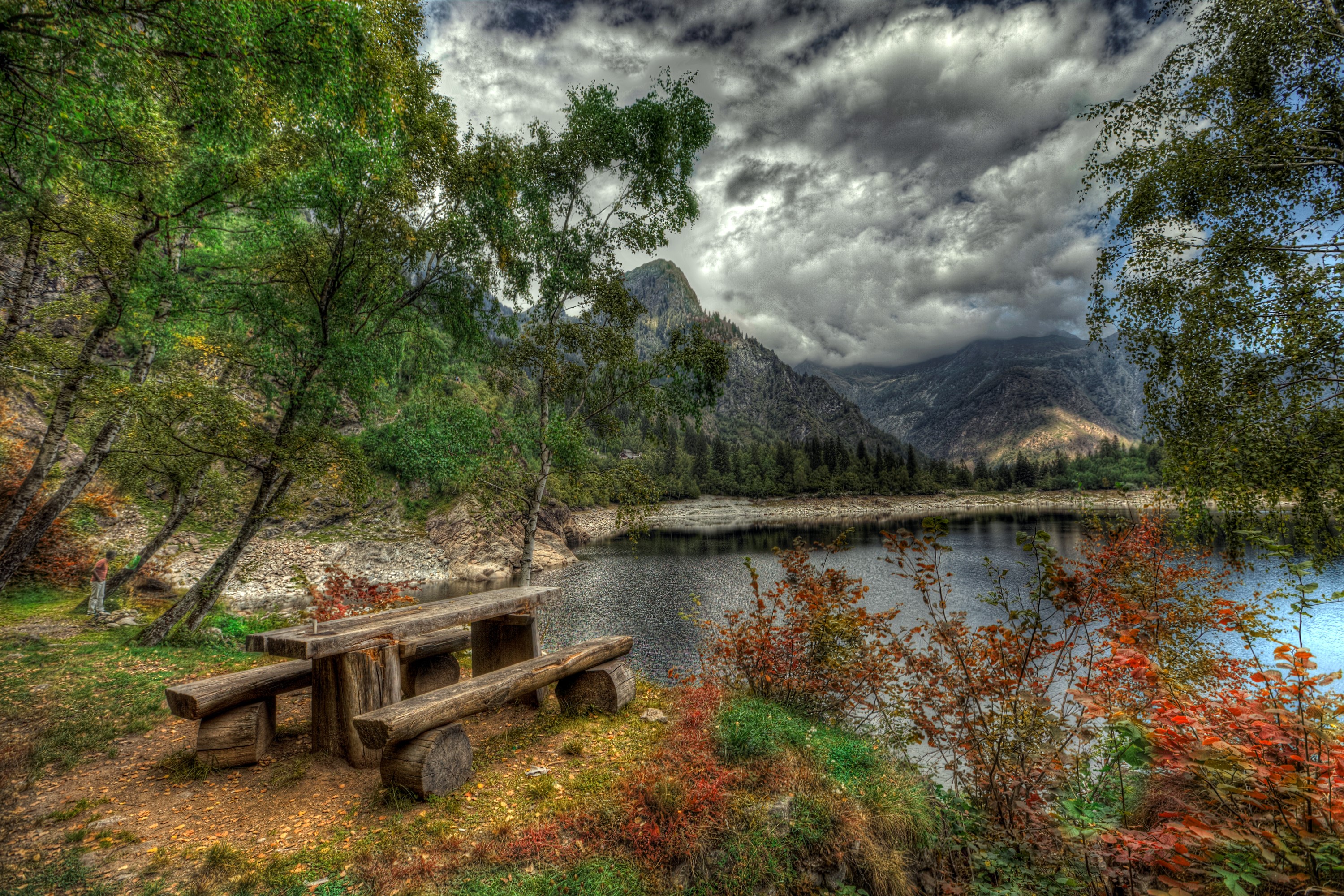 Wooden picnic table by a lake with mountains and clouds HD Wallpaper