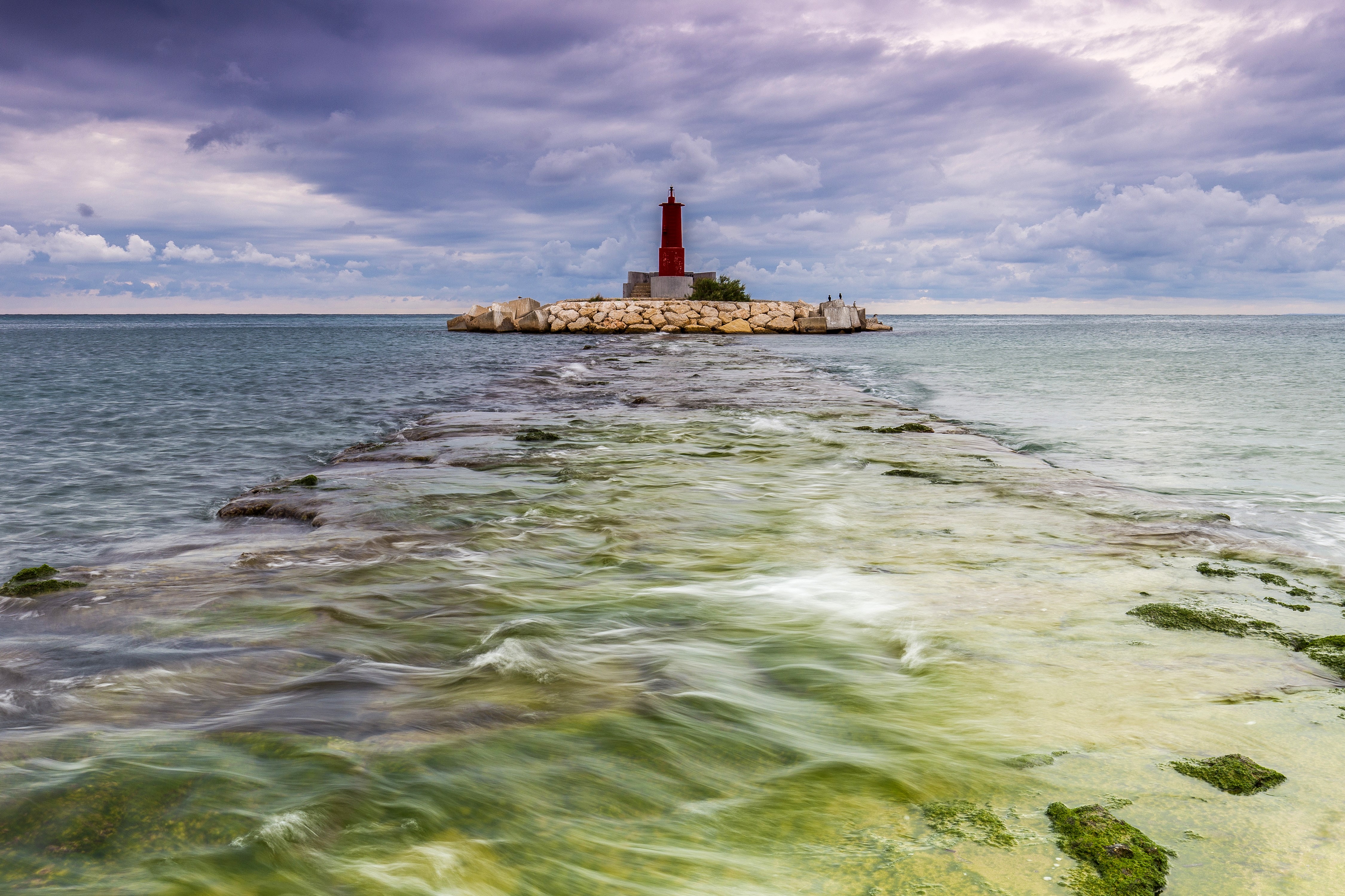 Red lighthouse on a rocky island in the sea HD Wallpaper