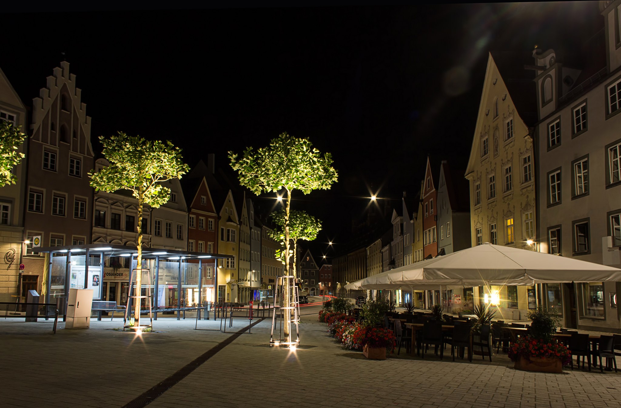 Street scene at night in Landsberg, Germany with illuminated trees and outdoor cafe HD Wallpaper