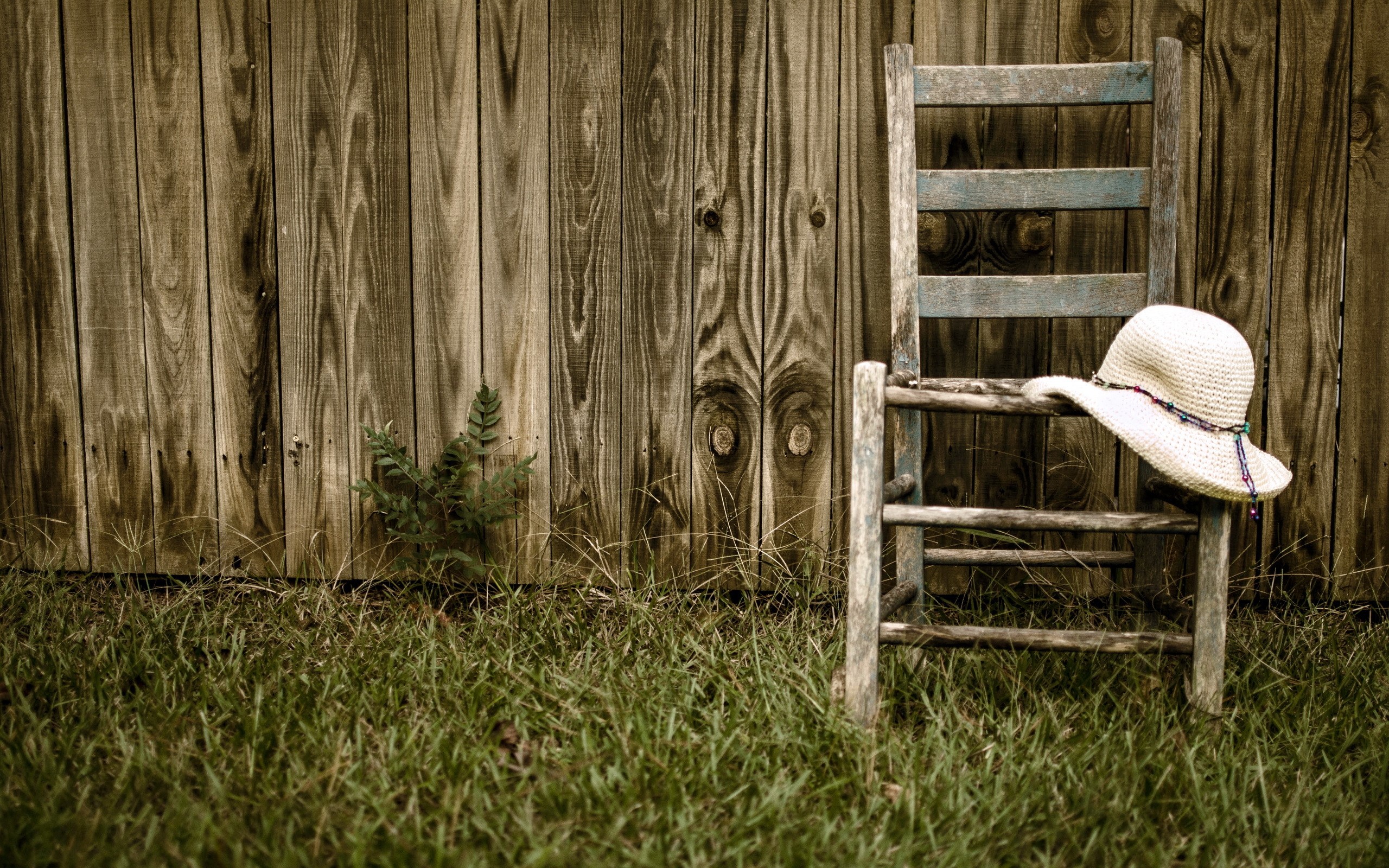 Old wooden chair with a straw hat by a fence HD Wallpaper