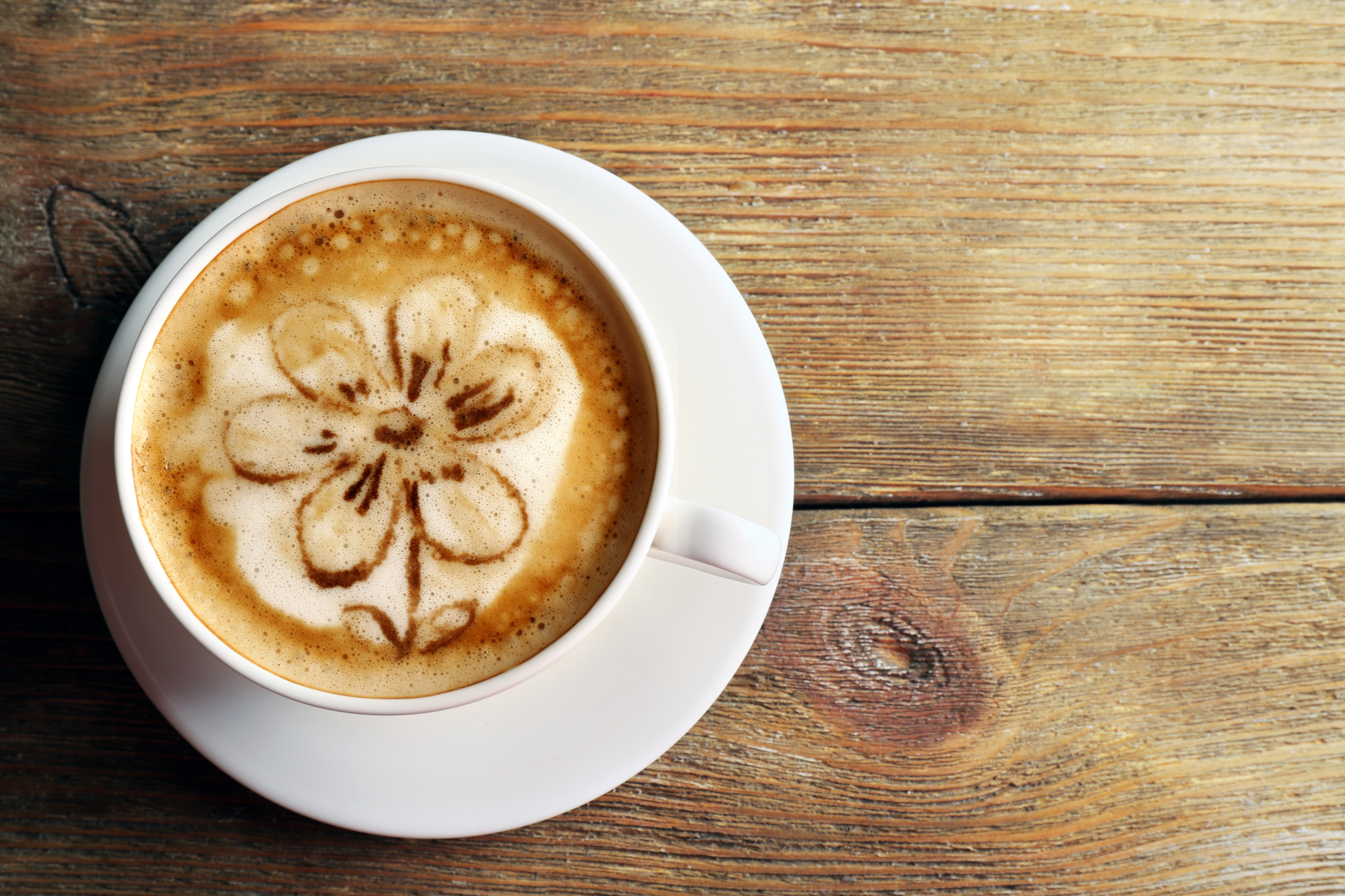 Cappuccino with flower art on wooden table HD Wallpaper