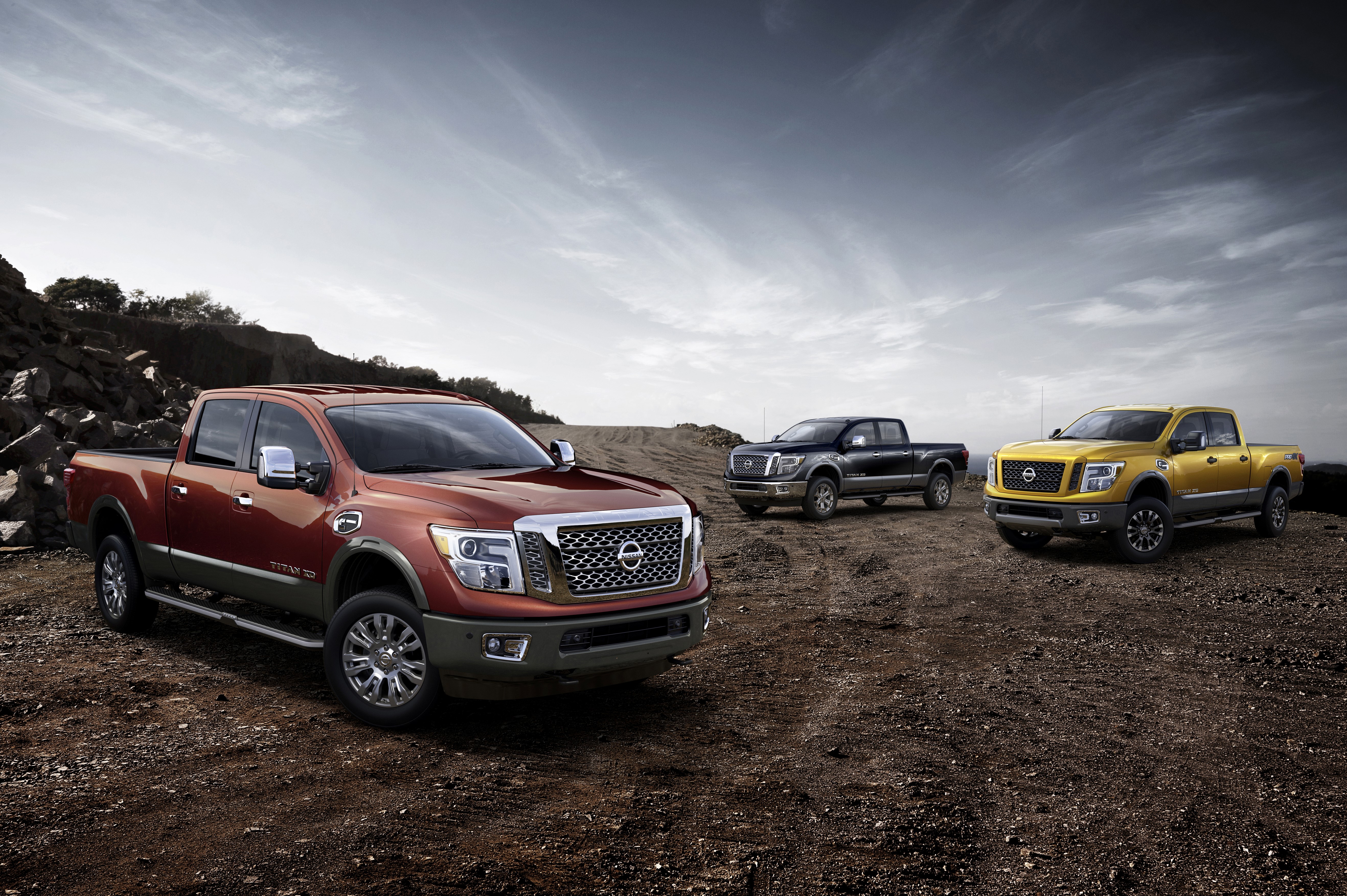 Three Nissan Titan XD trucks in a rocky landscape HD Wallpaper