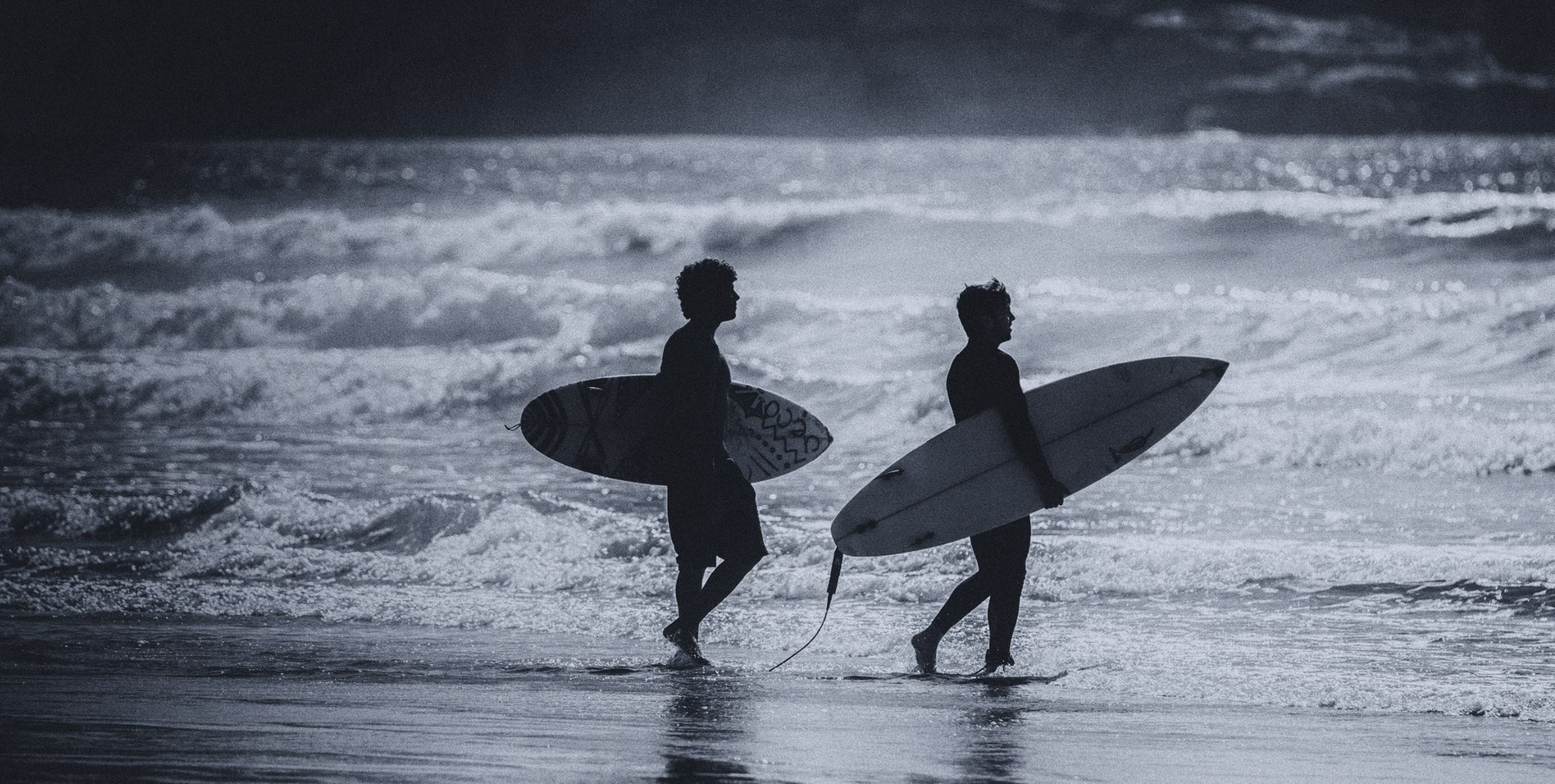 Two surfers walking on the beach with surfboards HD Wallpaper
