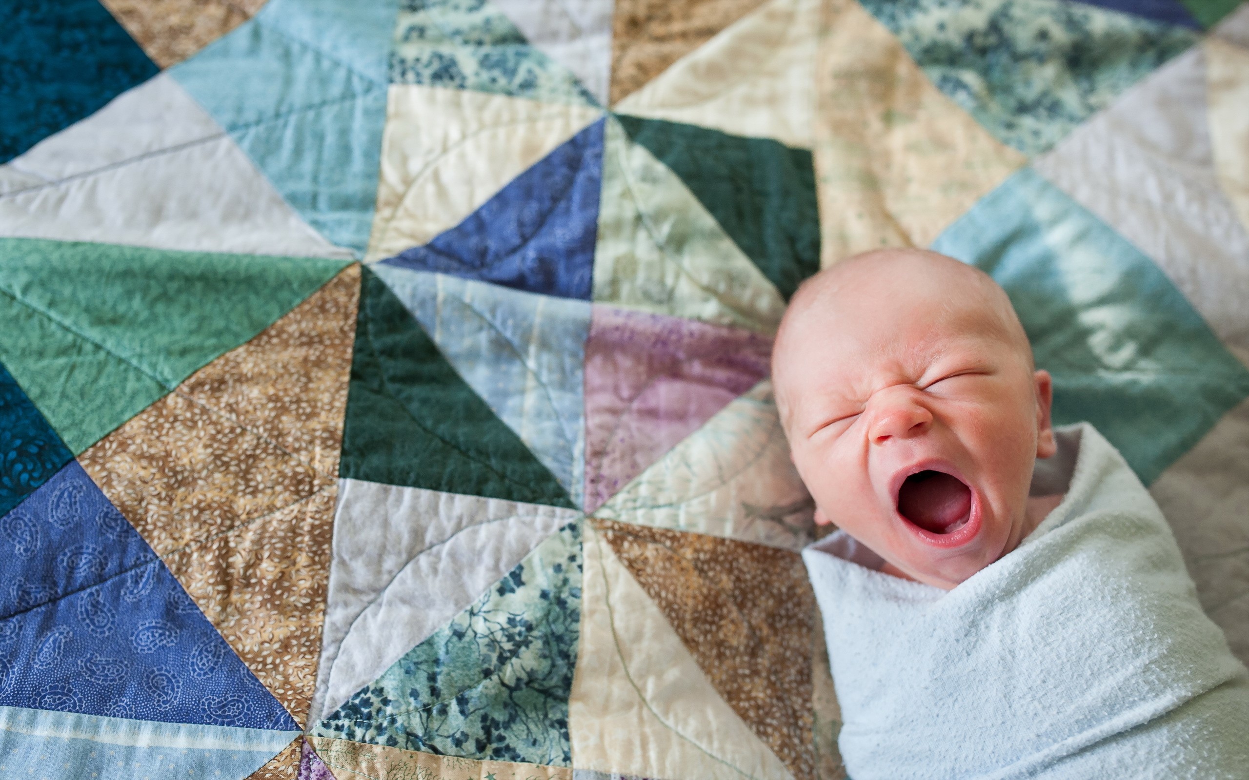 Newborn baby yawning on a colorful quilt HD Wallpaper