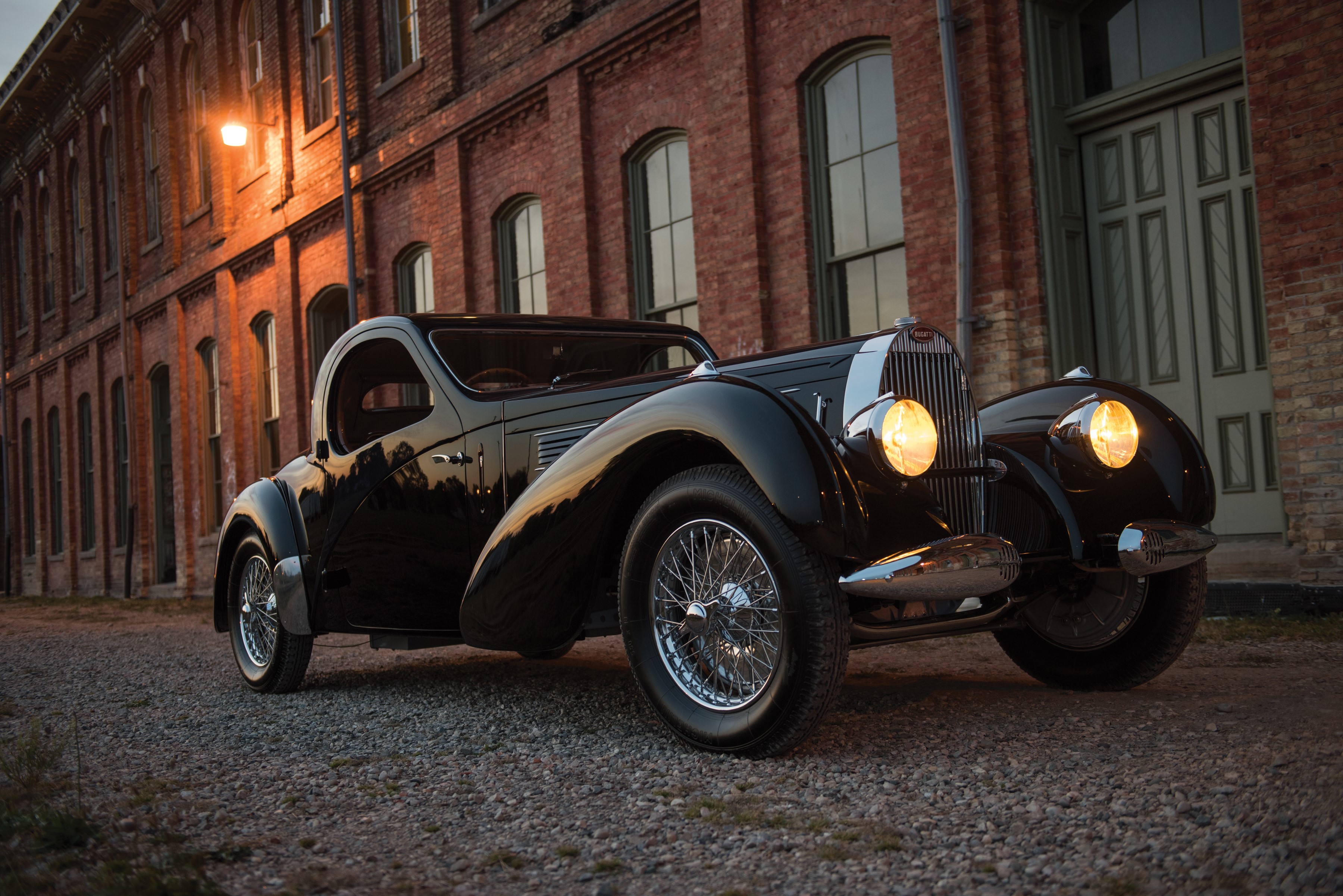 Black 1938 Bugatti Atalante parked outside brick building HD Wallpaper