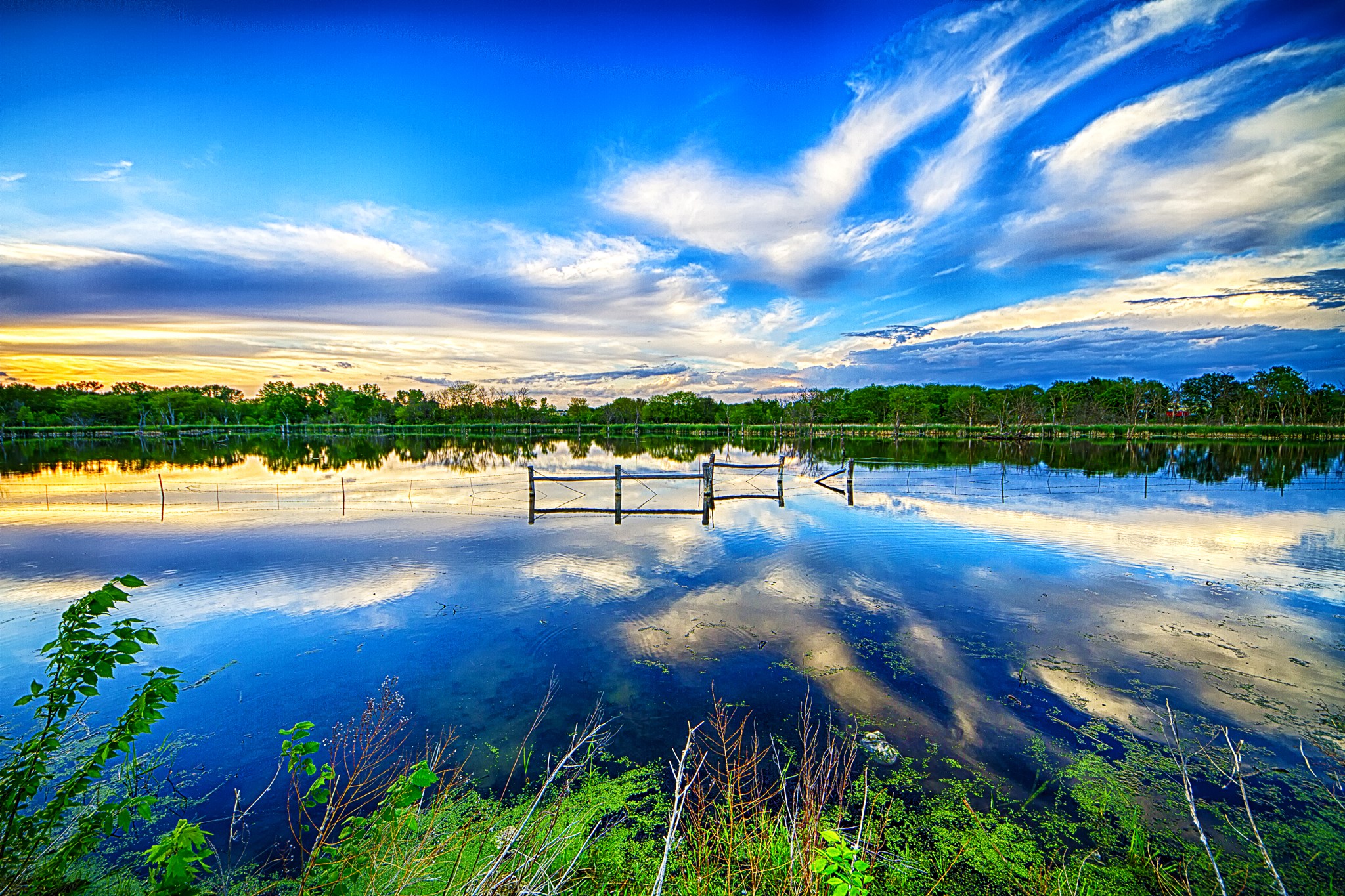 Lake with wooden fence and reflections under a cloudy sky HD Wallpaper