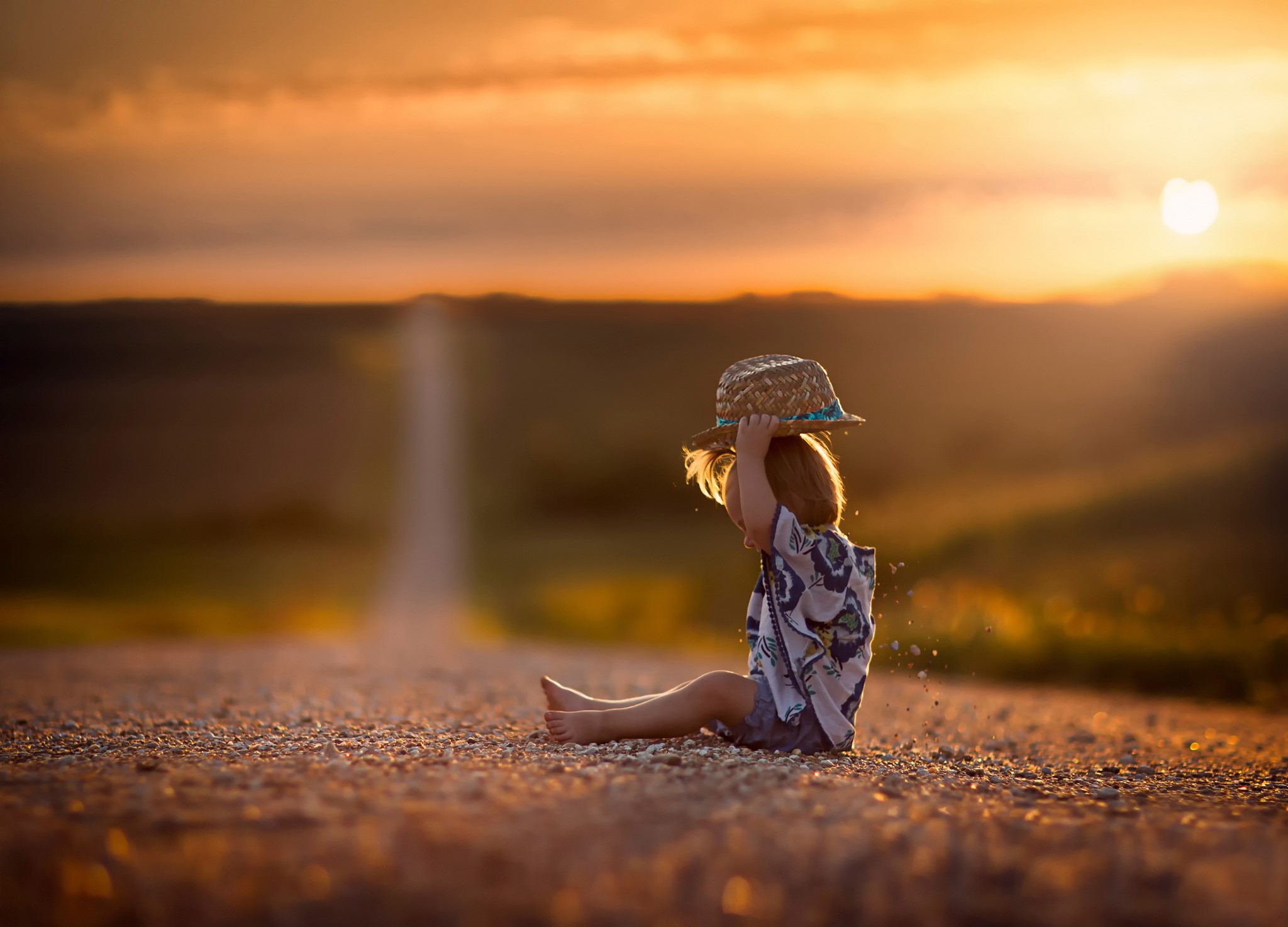 Child in straw hat sitting on a road at sunset HD Wallpaper