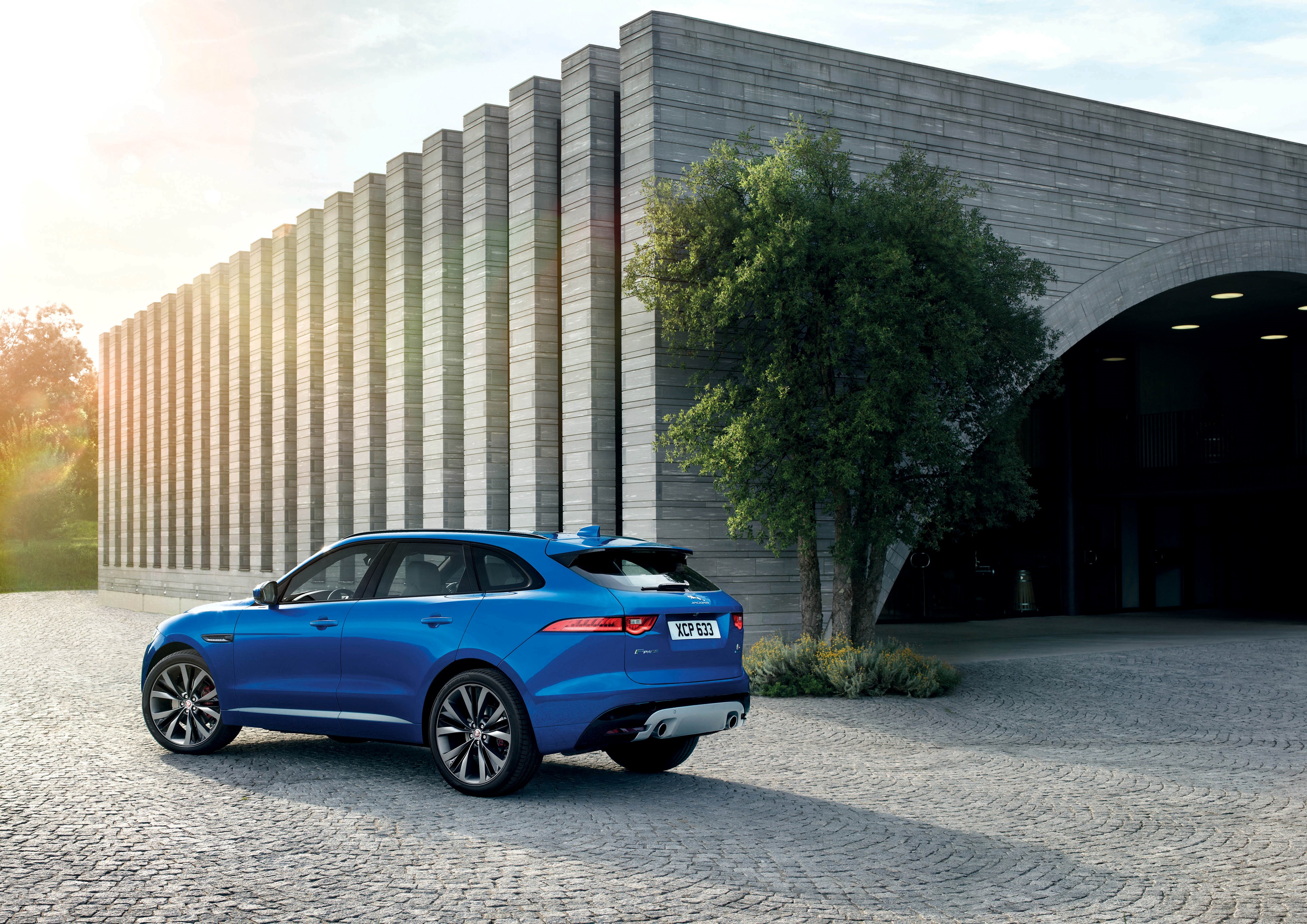Blue Jaguar F-Pace parked in front of a modern building HD Wallpaper