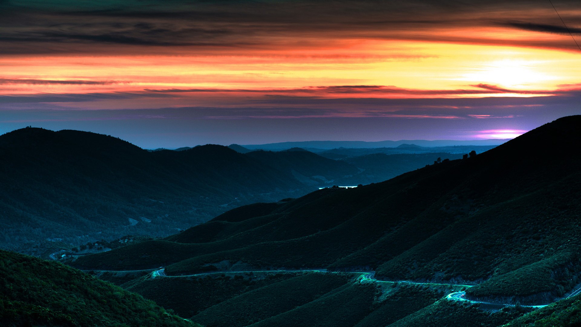 Mountain range at sunset with winding road HD Wallpaper
