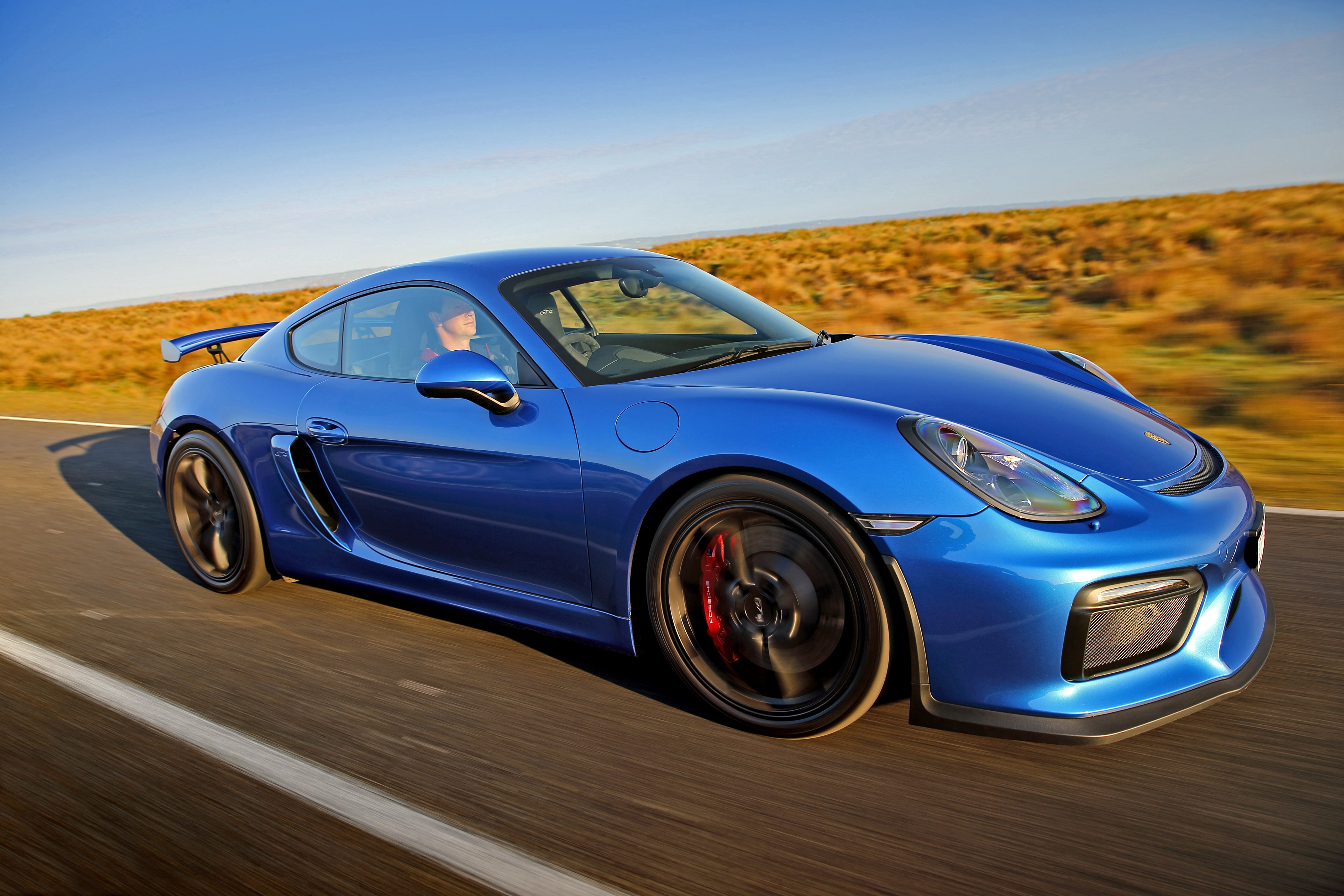 Blue Porsche Cayman GT4 driving on a road HD Wallpaper