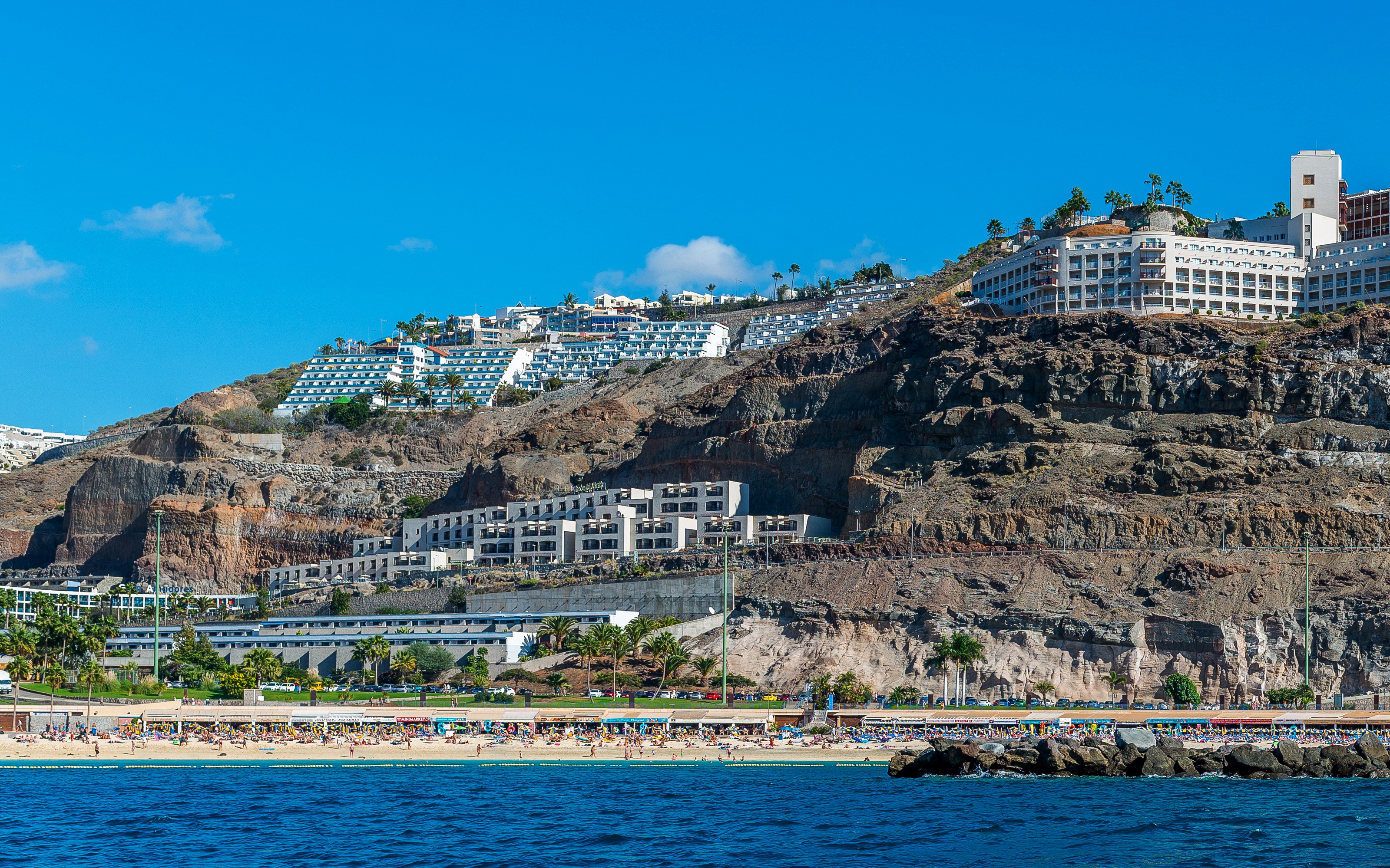 Hotels on a rocky hillside overlooking a beach in Puerto Rico, Gran Canaria HD Wallpaper