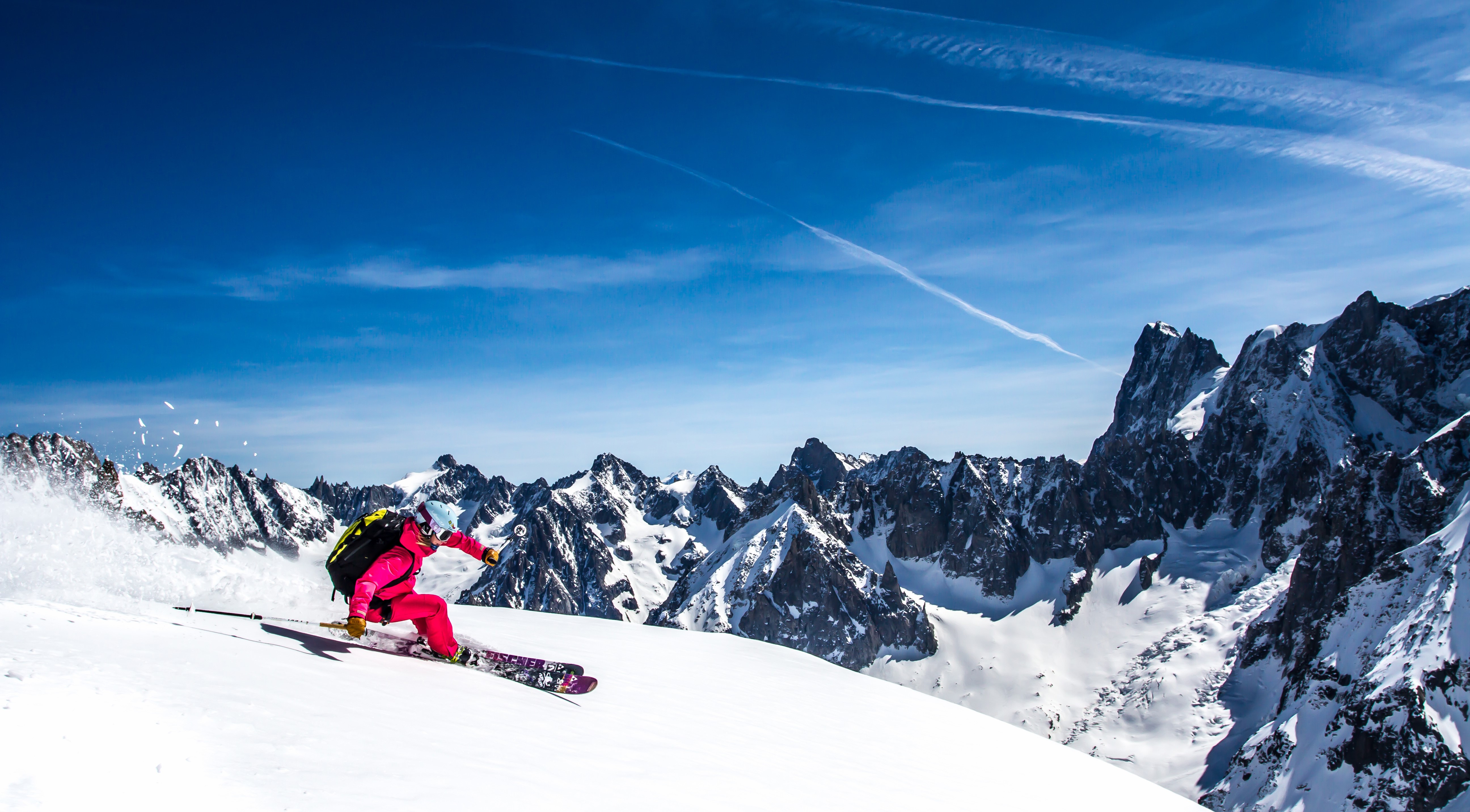 Skiing down a snowy mountain under a blue sky HD Wallpaper