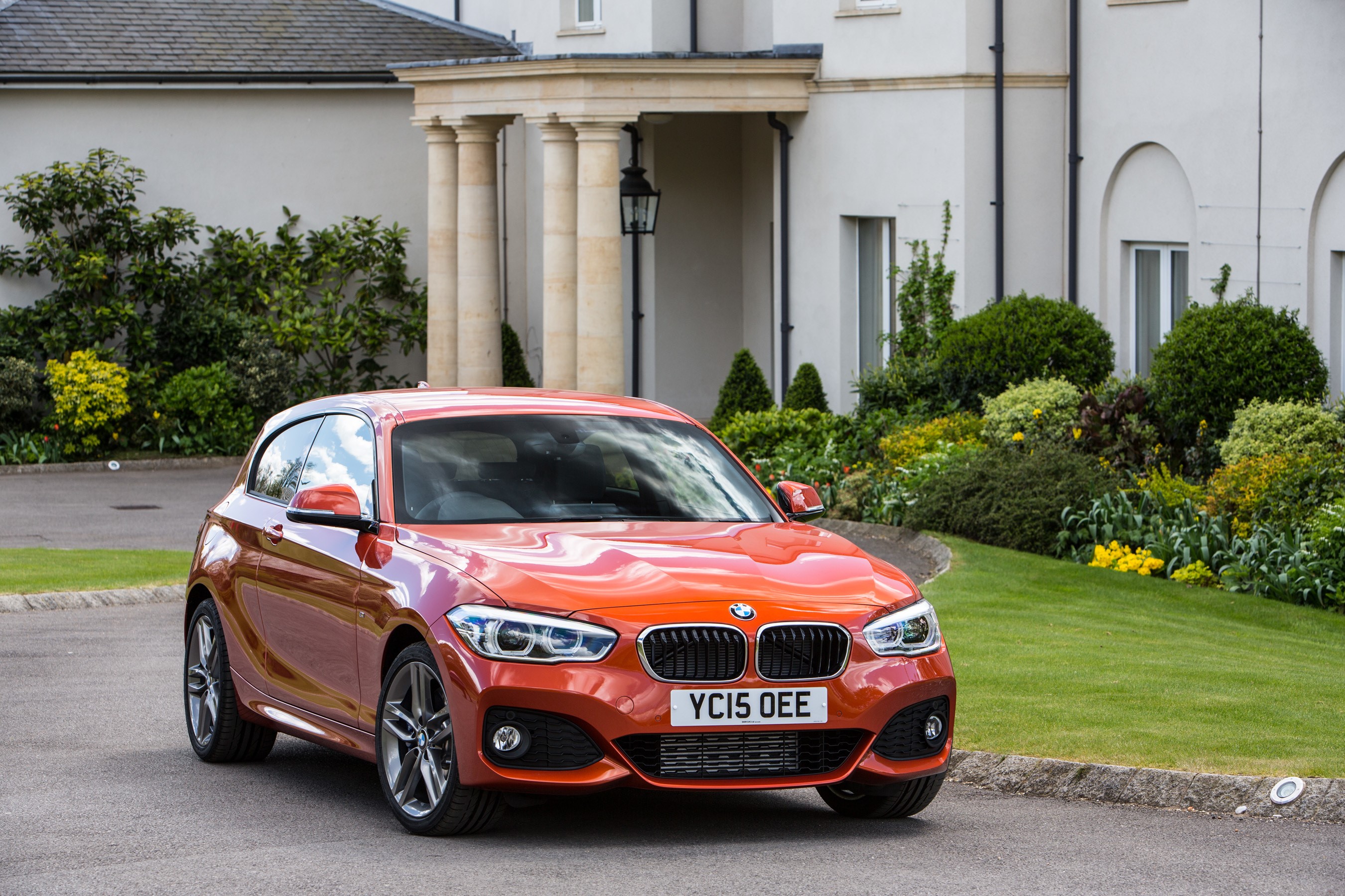 Orange BMW M120i Sport 3-door parked in front of a house HD Wallpaper