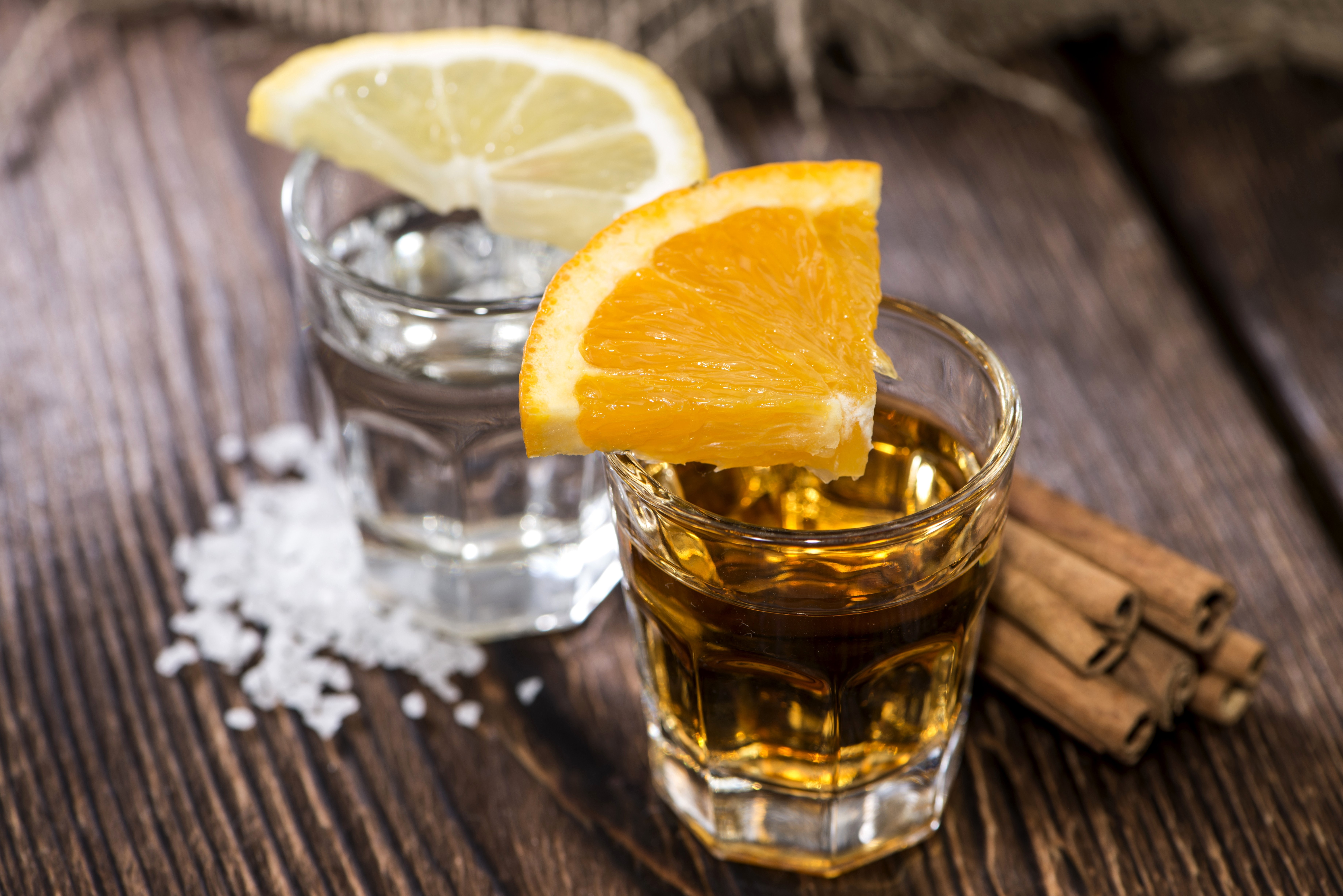Two shot glasses with tequila and vodka, garnished with orange and lemon slices, with cinnamon sticks and salt HD Wallpaper