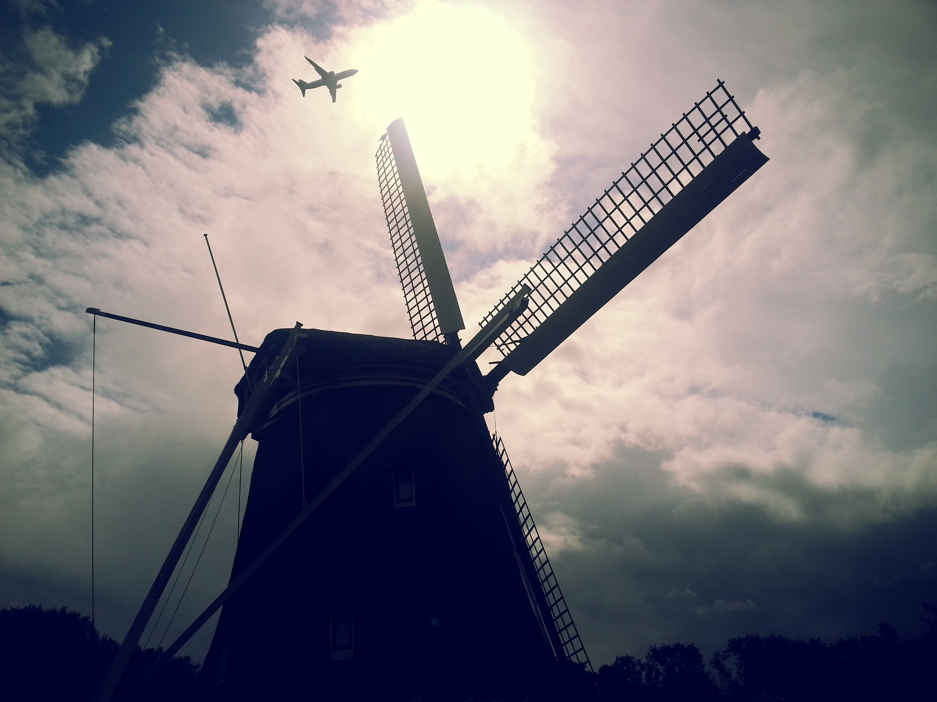 Airplane flying over a windmill against cloudy sky HD Wallpaper