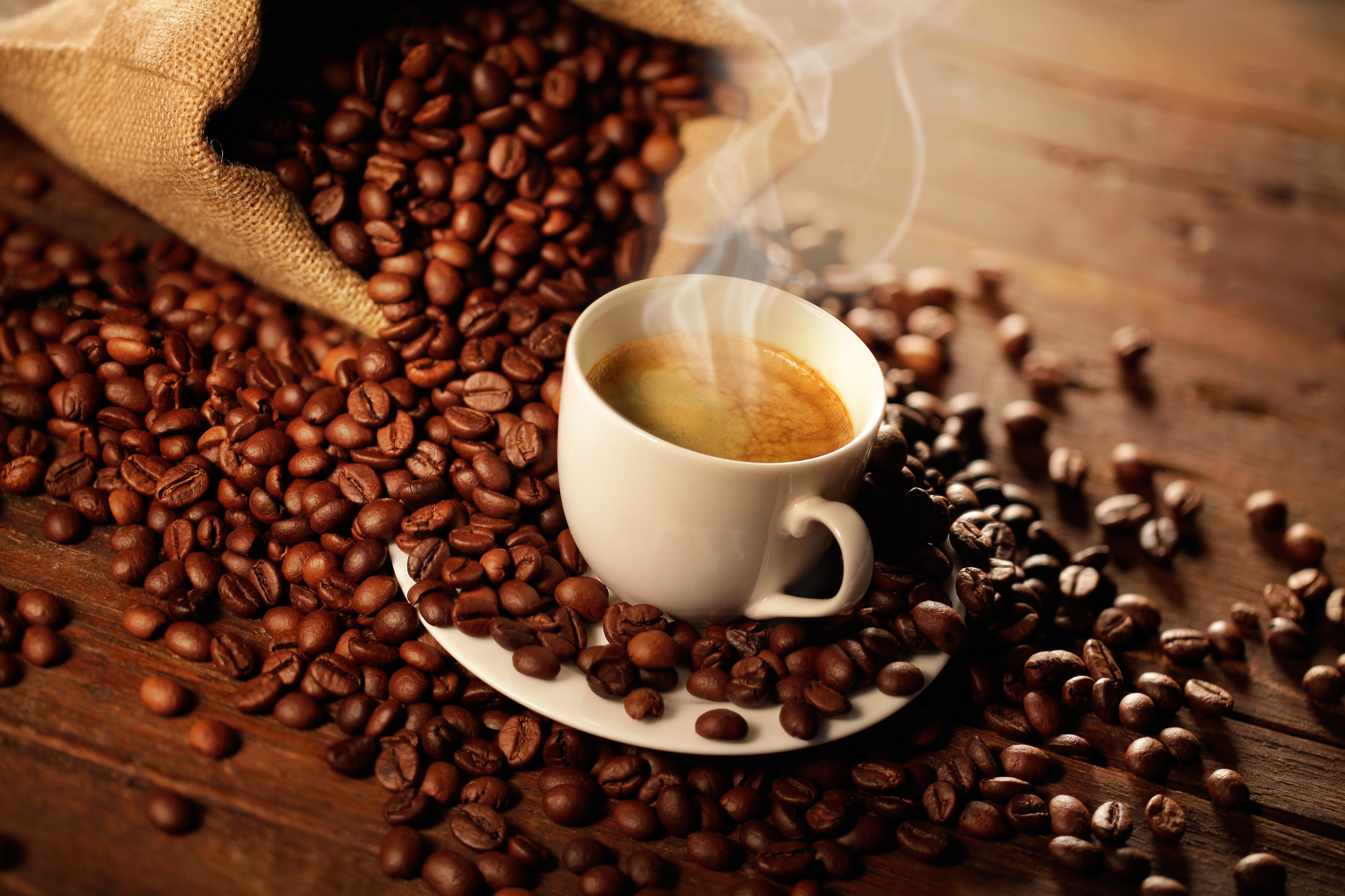 Coffee beans spilling from a burlap sack next to a steaming cup of coffee HD Wallpaper