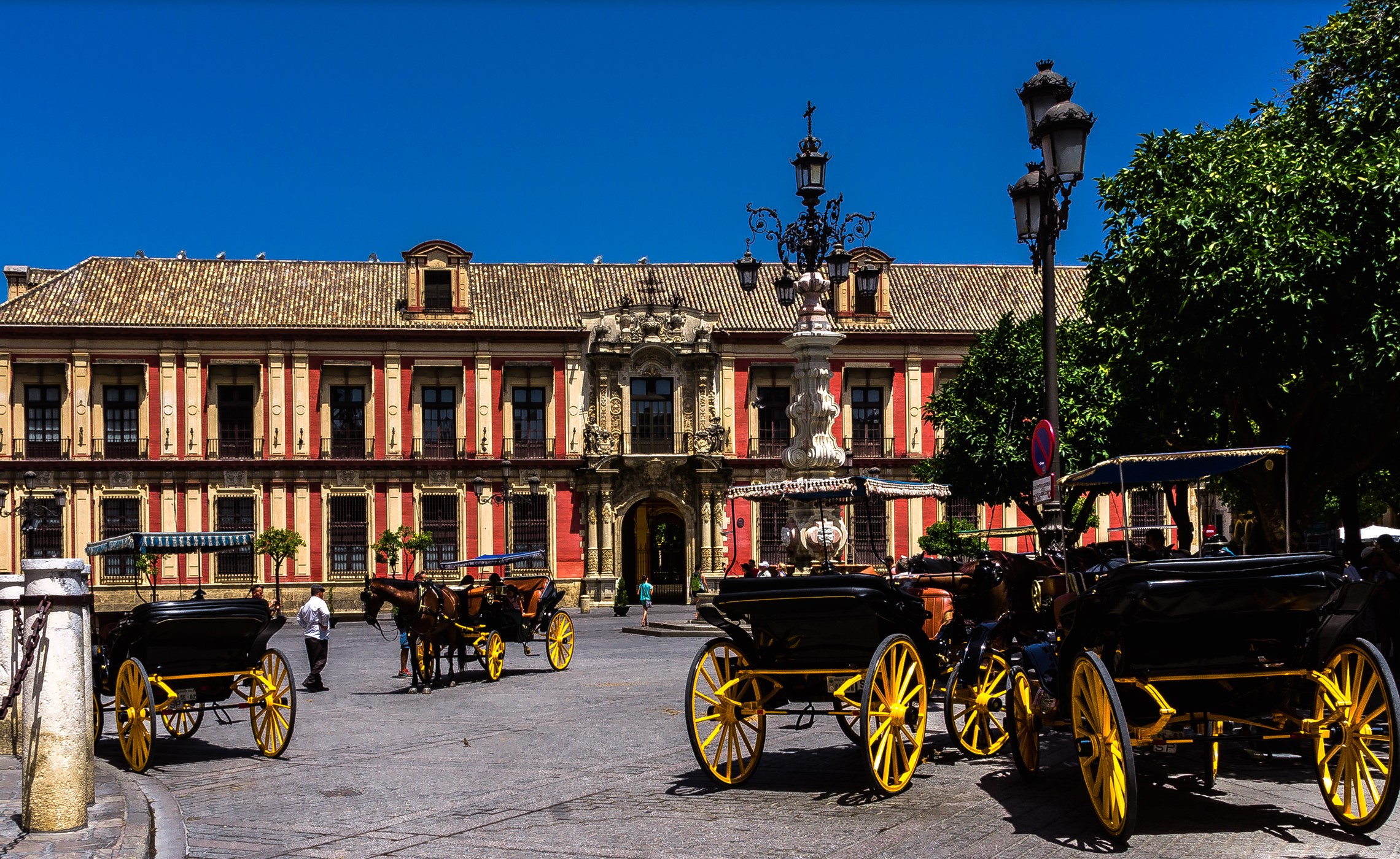 Horse-drawn carriages in front of a historic building in Seville HD Wallpaper