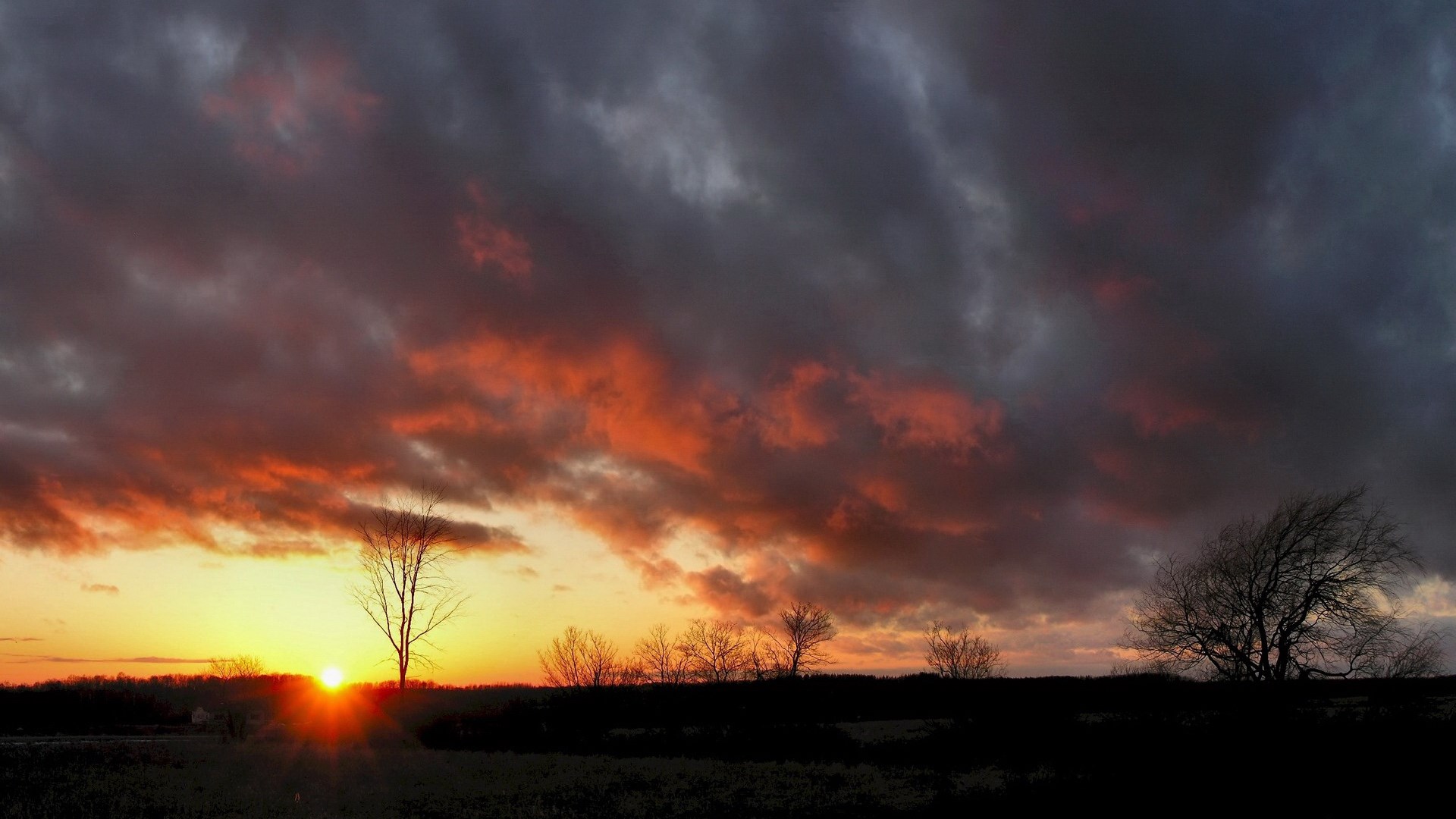 Sunset with dramatic clouds over a silhouetted landscape HD Wallpaper