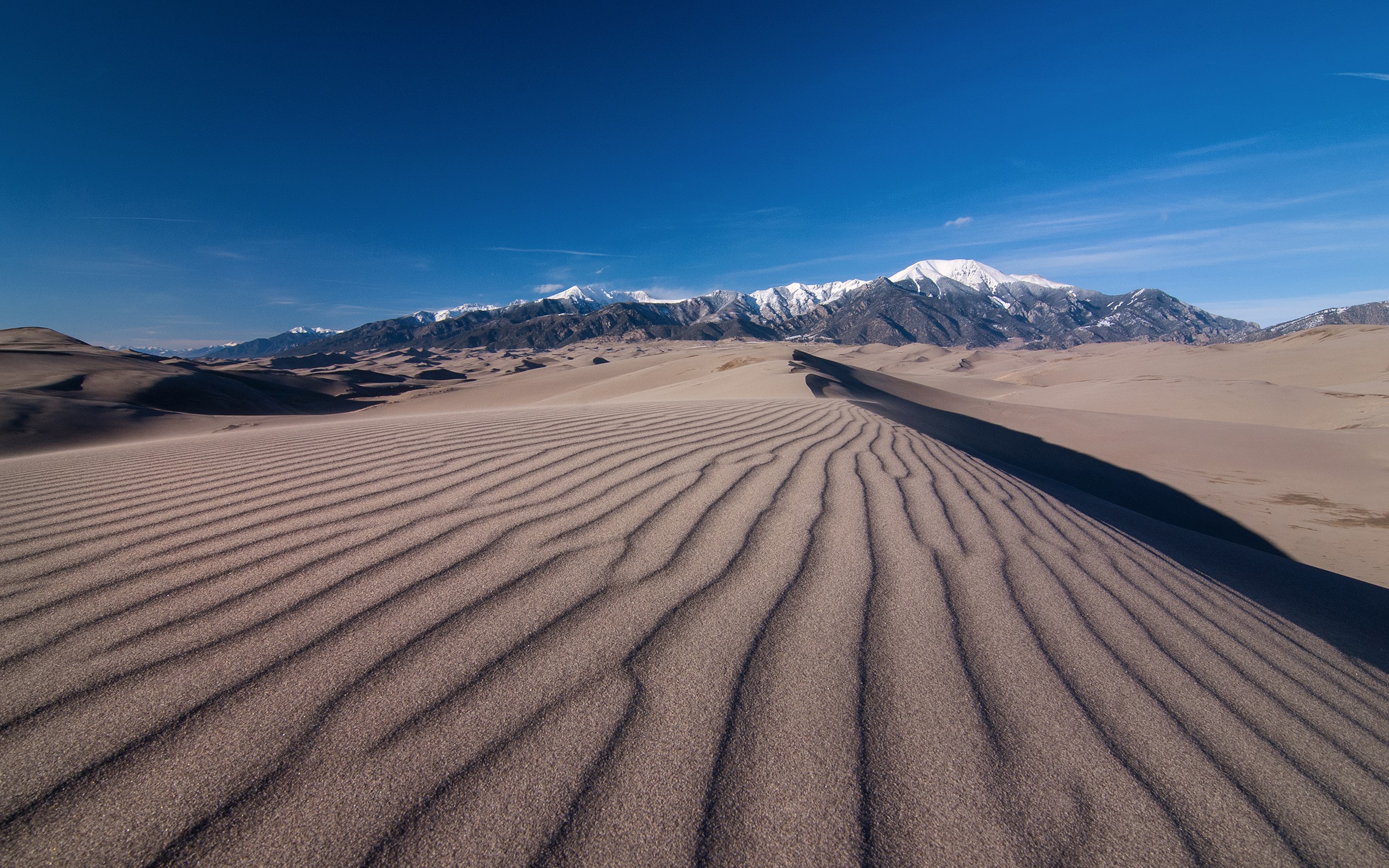 Sand dunes with snow-capped mountains under a blue sky HD Wallpaper