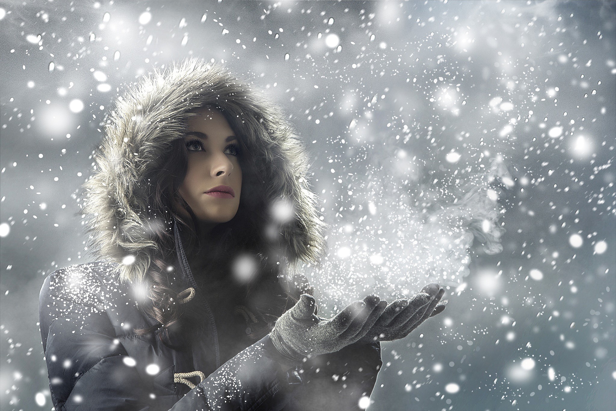 Woman in fur-hooded coat blowing snow from hands HD Wallpaper