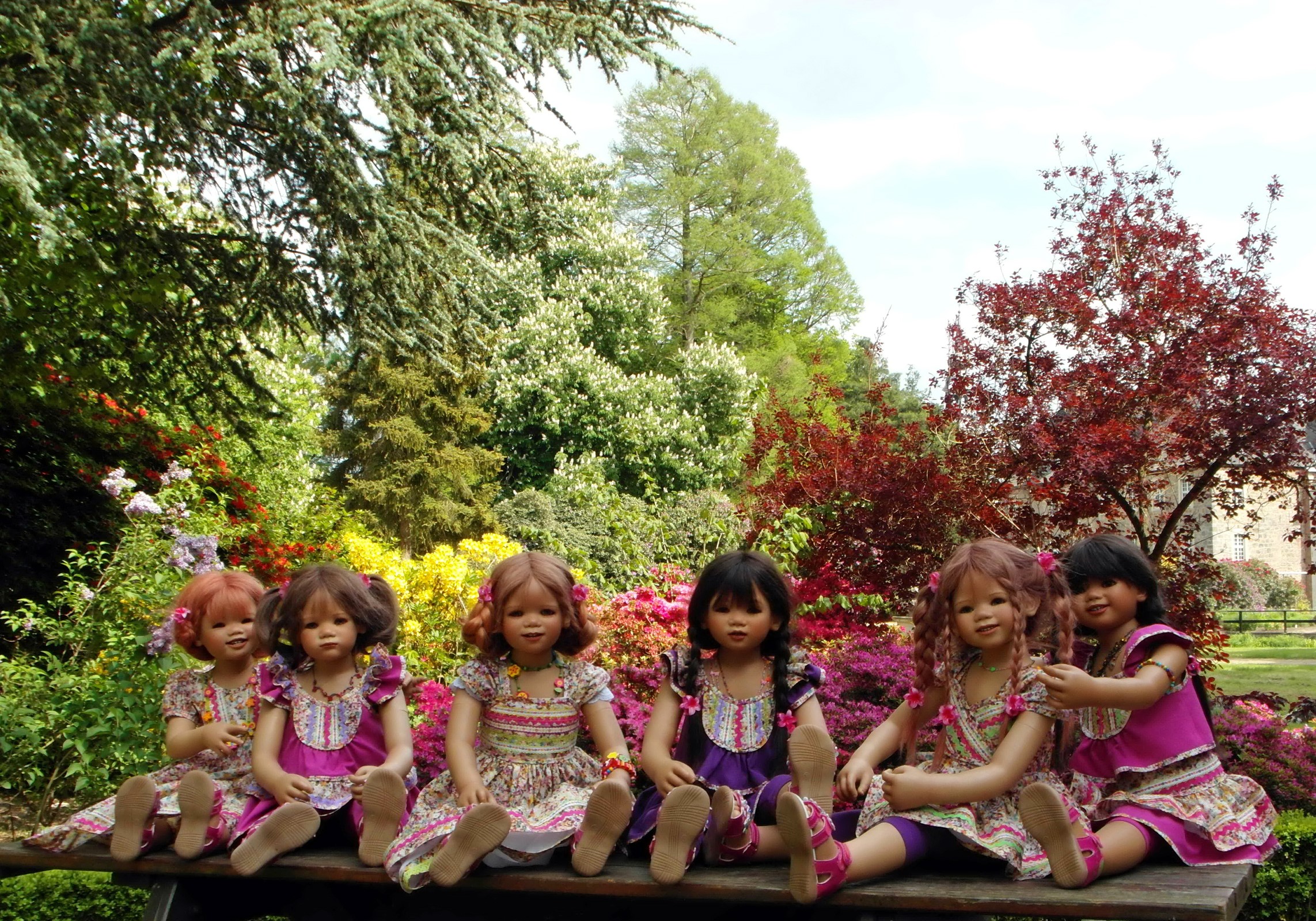 Dolls in dresses sitting on a bench in a garden HD Wallpaper